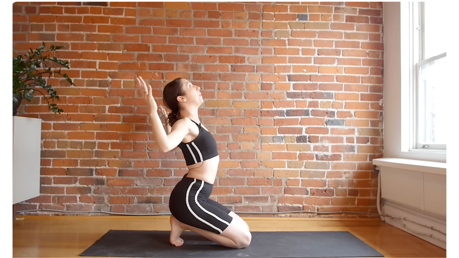 Yoga teacher kneeling on a mat with her toes tucked and her arms bent in a cactus shape