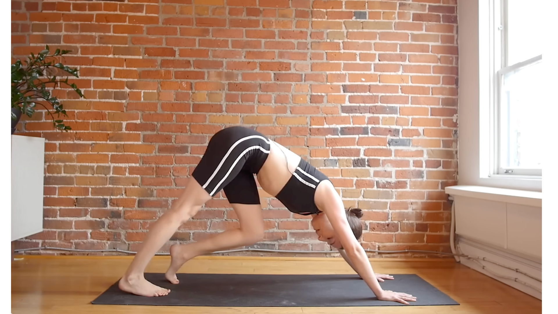 Yoga teacher practicing Downward-Facing Dog on a yoga mat during a 10-minute morning yoga stretches routine that focuses on a full-body stretch.