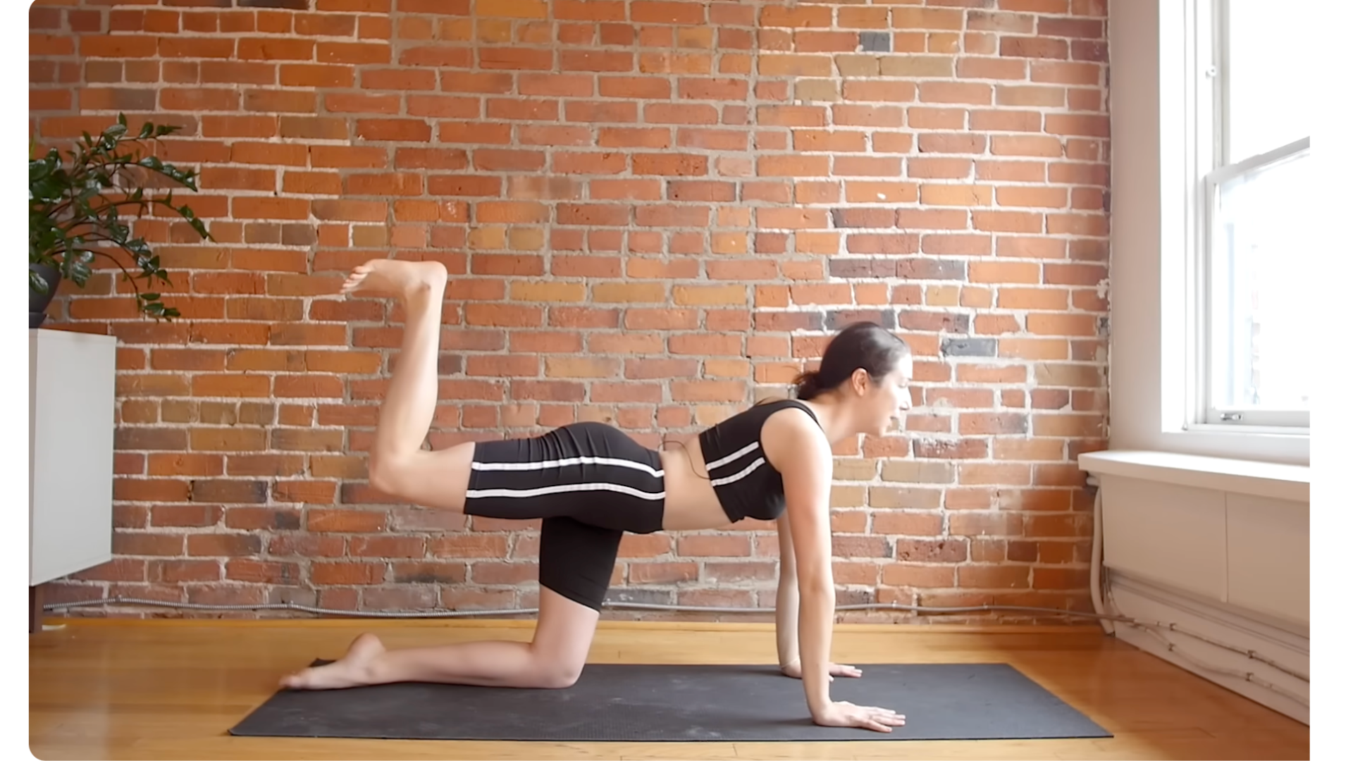 Yoga teacher kneeling on a mat with shoulders over wrists and hips over knees with her right knee lifted and her foot reaching toward the ceiling