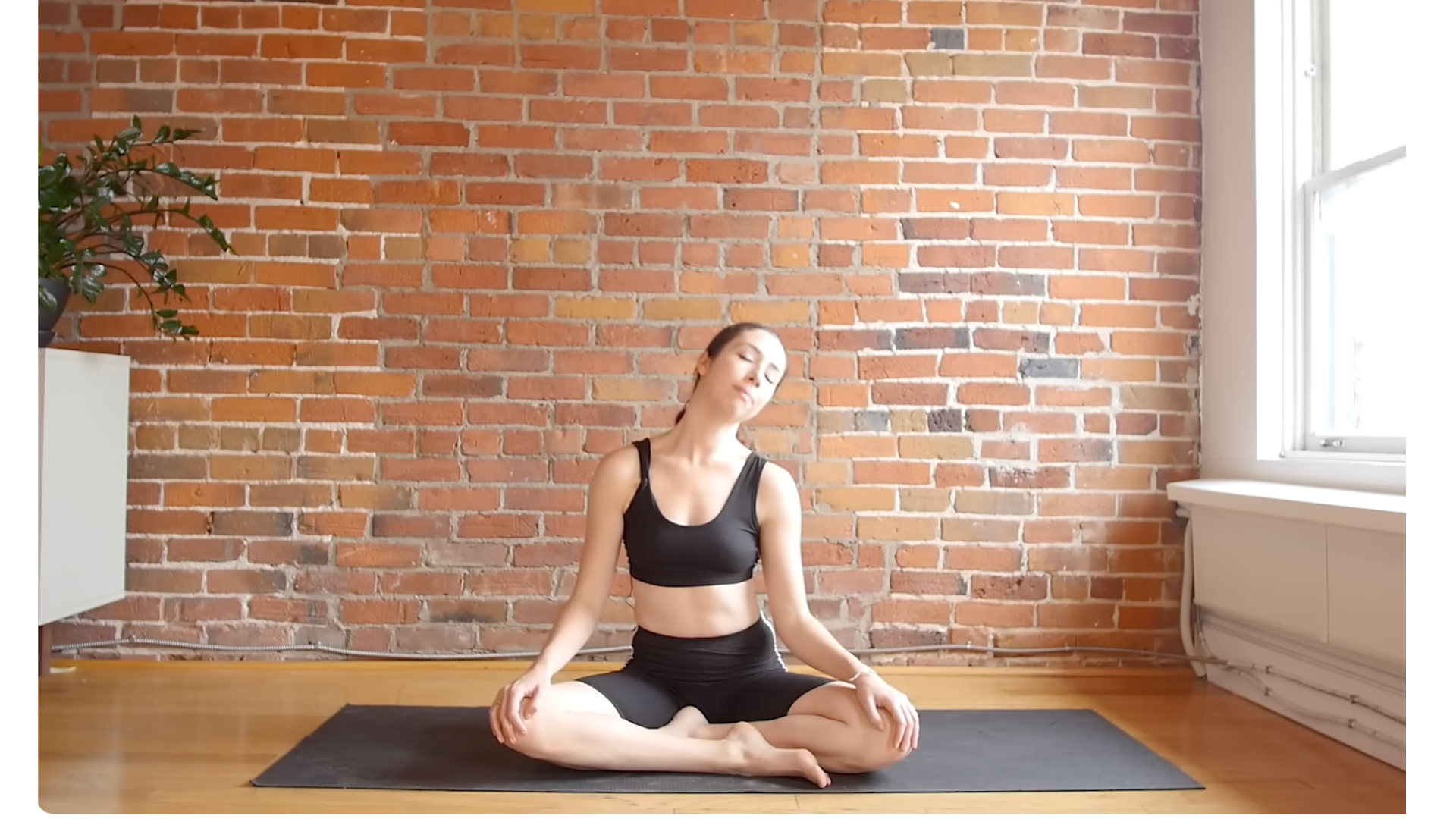Yoga teacher sitting on a mat leaning her head to one side in a gentle neck stretch