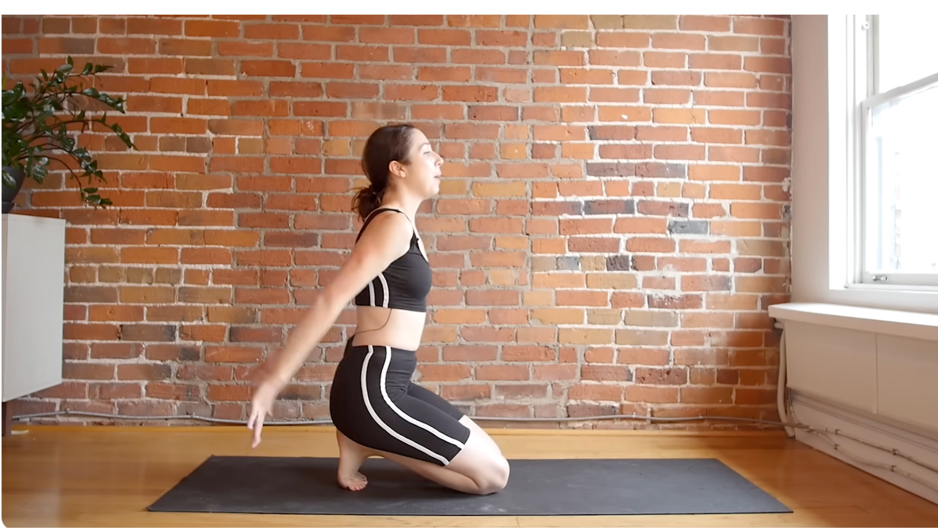 Yoga teacher kneeling on a mat sweeping her arms behind her during shoulder stretches