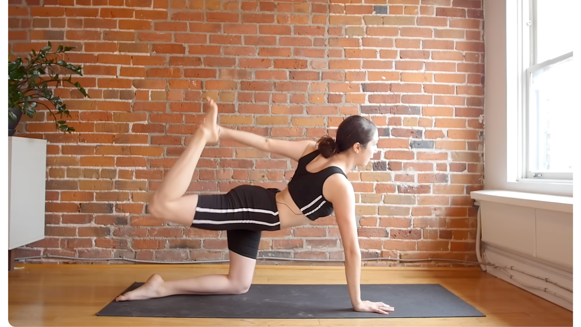 Yoga teacher kneeling on a mat reaching her left hand behind her to reach for her right foot during a full-body stretch