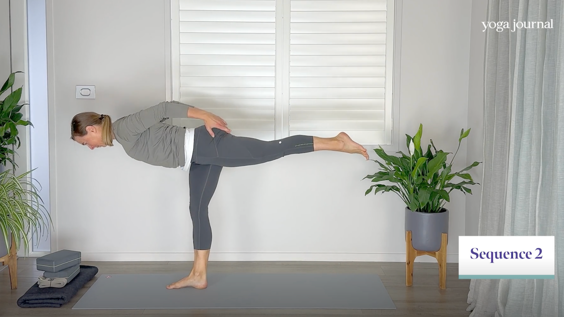 Yoga teacher practicing Warrior 3 on a yoga mat with one leg extended straight behind her during a yoga cardio exercise