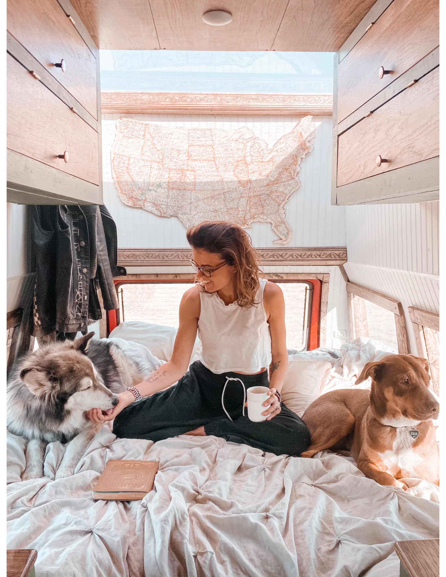 Writer Sierra Vandervort sitting on a bed with her dogs in her year of living in a van