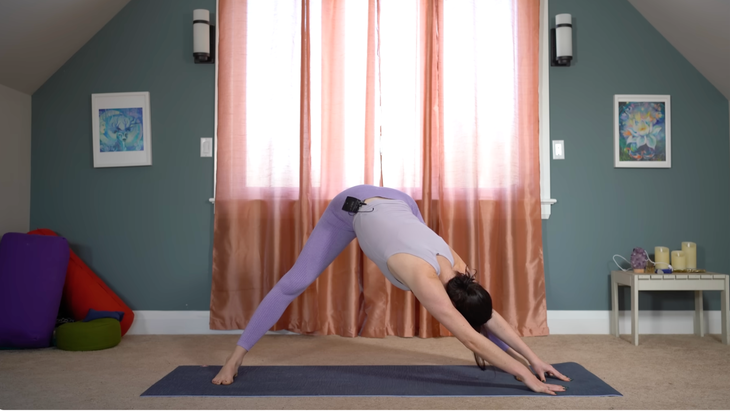 woman in wide-legged standing forward fold has left hands extending over to left foot