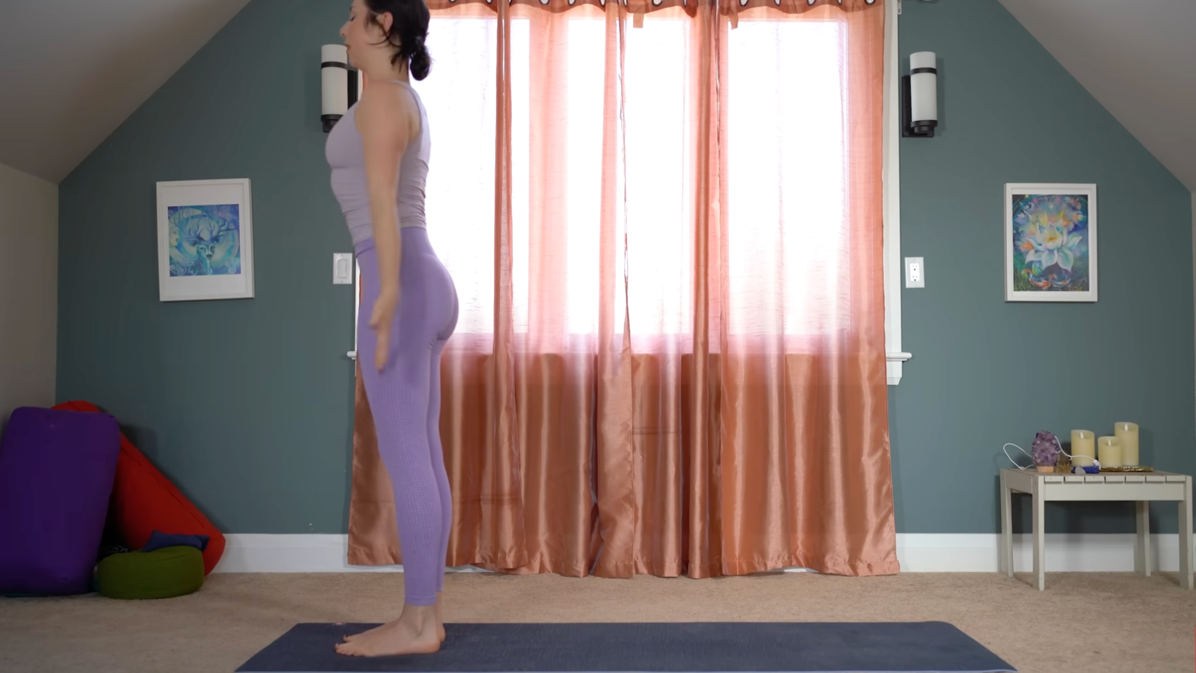 woman in purple yoga clothes stands in mountain pose at front of yoga mat