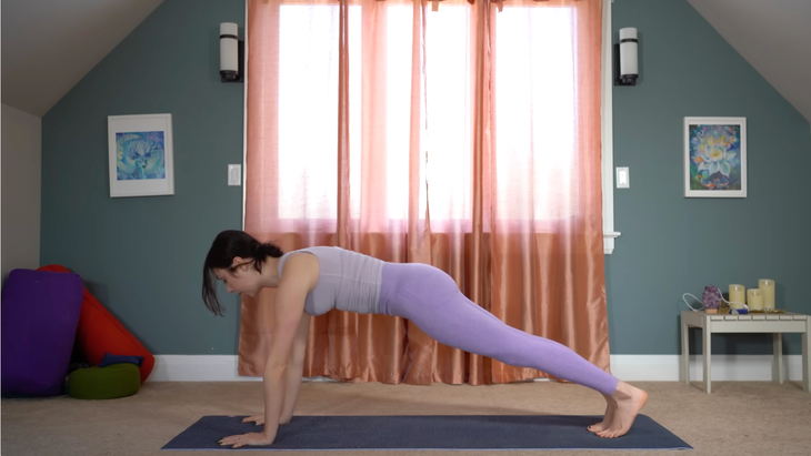 woman in purple yoga clothes in plank pose on mat in house in front of windows with closed curtains