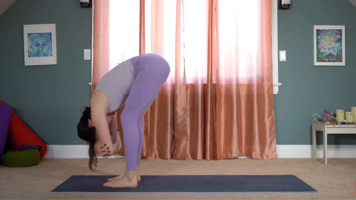 woman in standing forward bend yoga pose at front of mat with rag doll arms and knees slightly bent