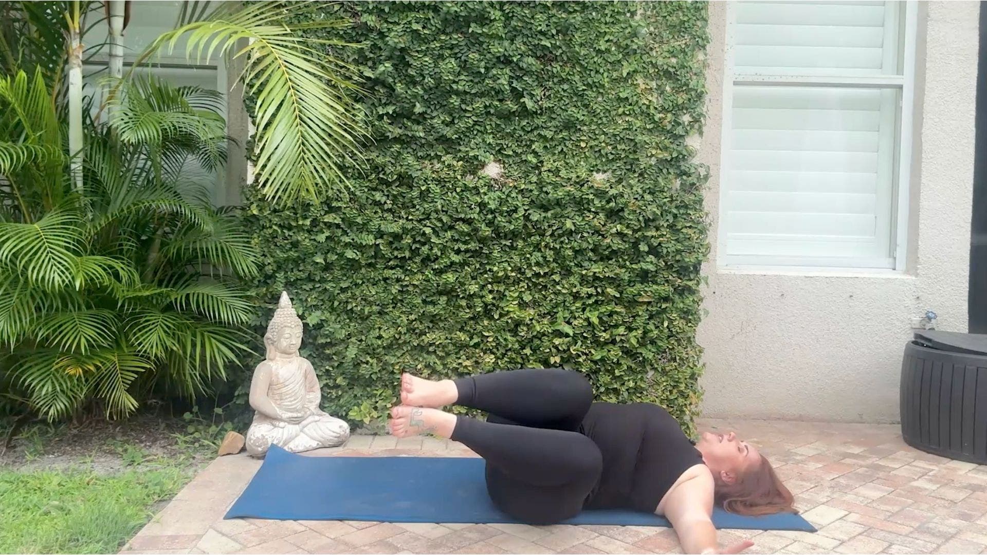 Woman on a yoga mat with her knees drawn toward her chest and toward the side.