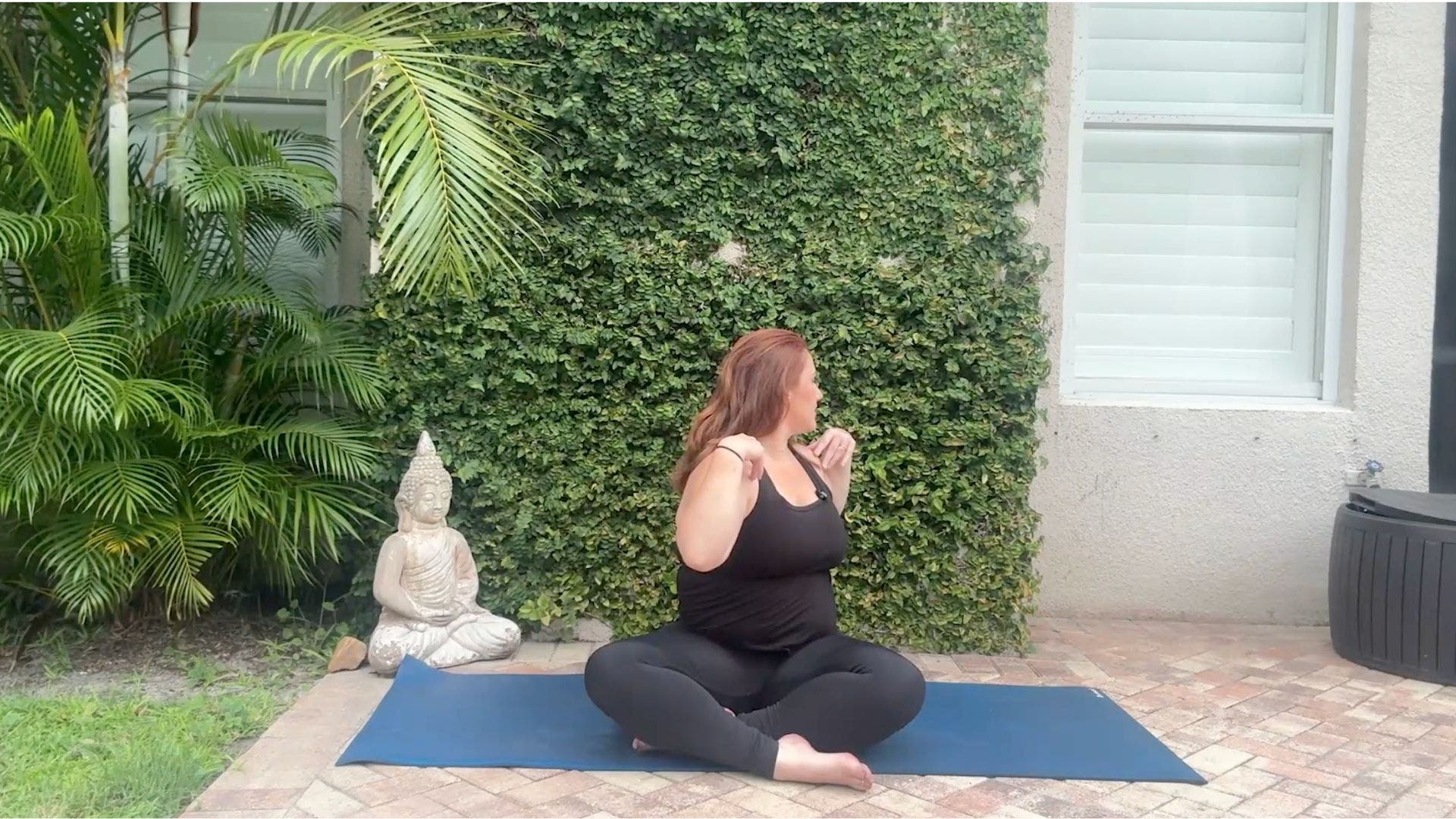 Woman sitting cross-legged on yoga mat twisting toward one side.