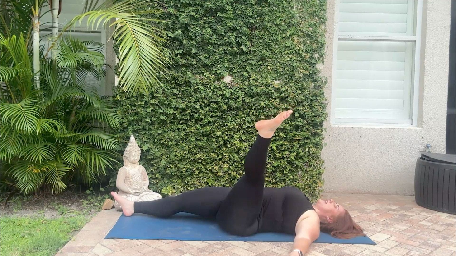 Woman lying on back on yoga mat with one leg extended in the air.