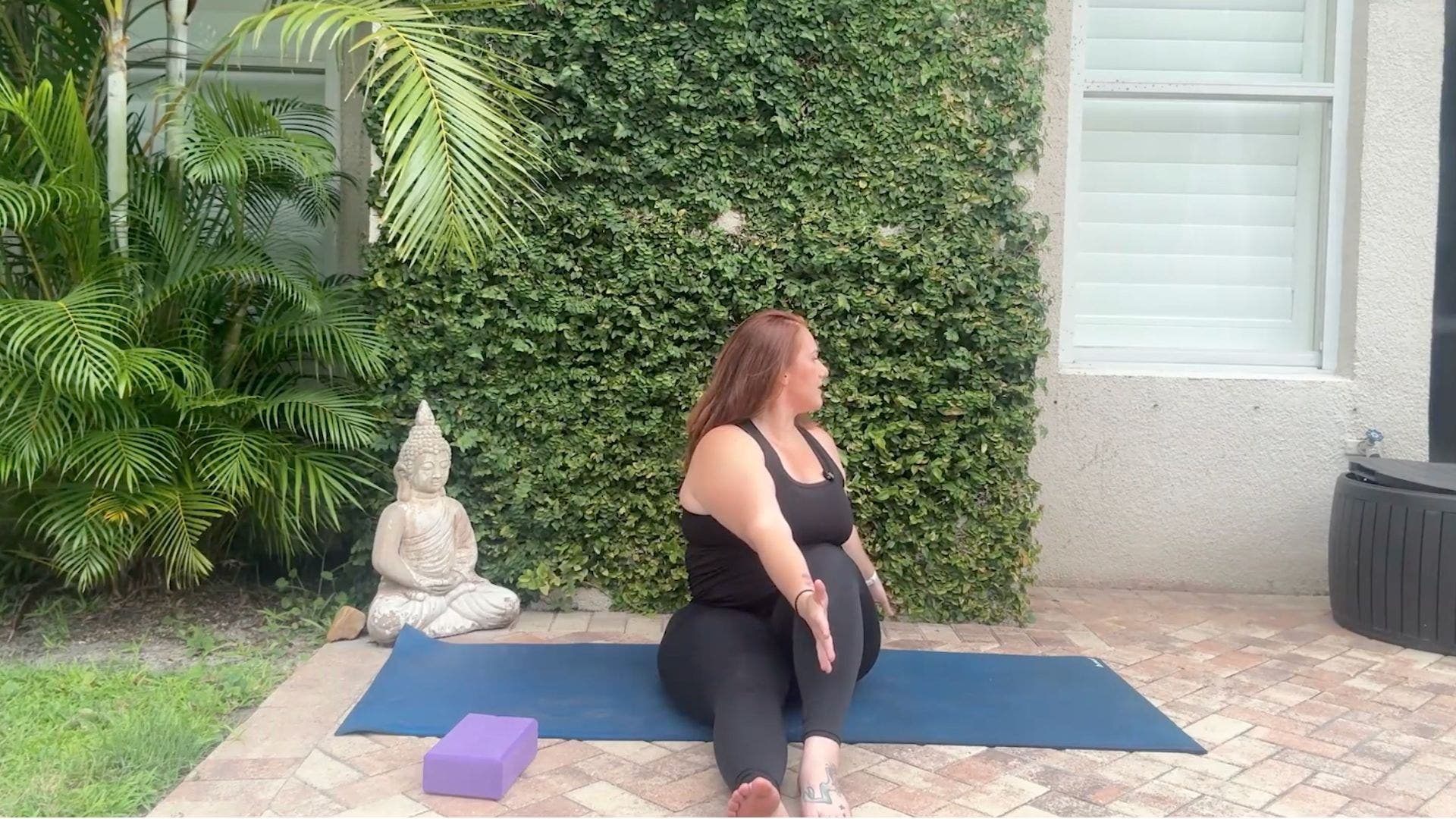 Woman sitting on yoga mat with one leg straight and one leg bent, twisting toward one side.