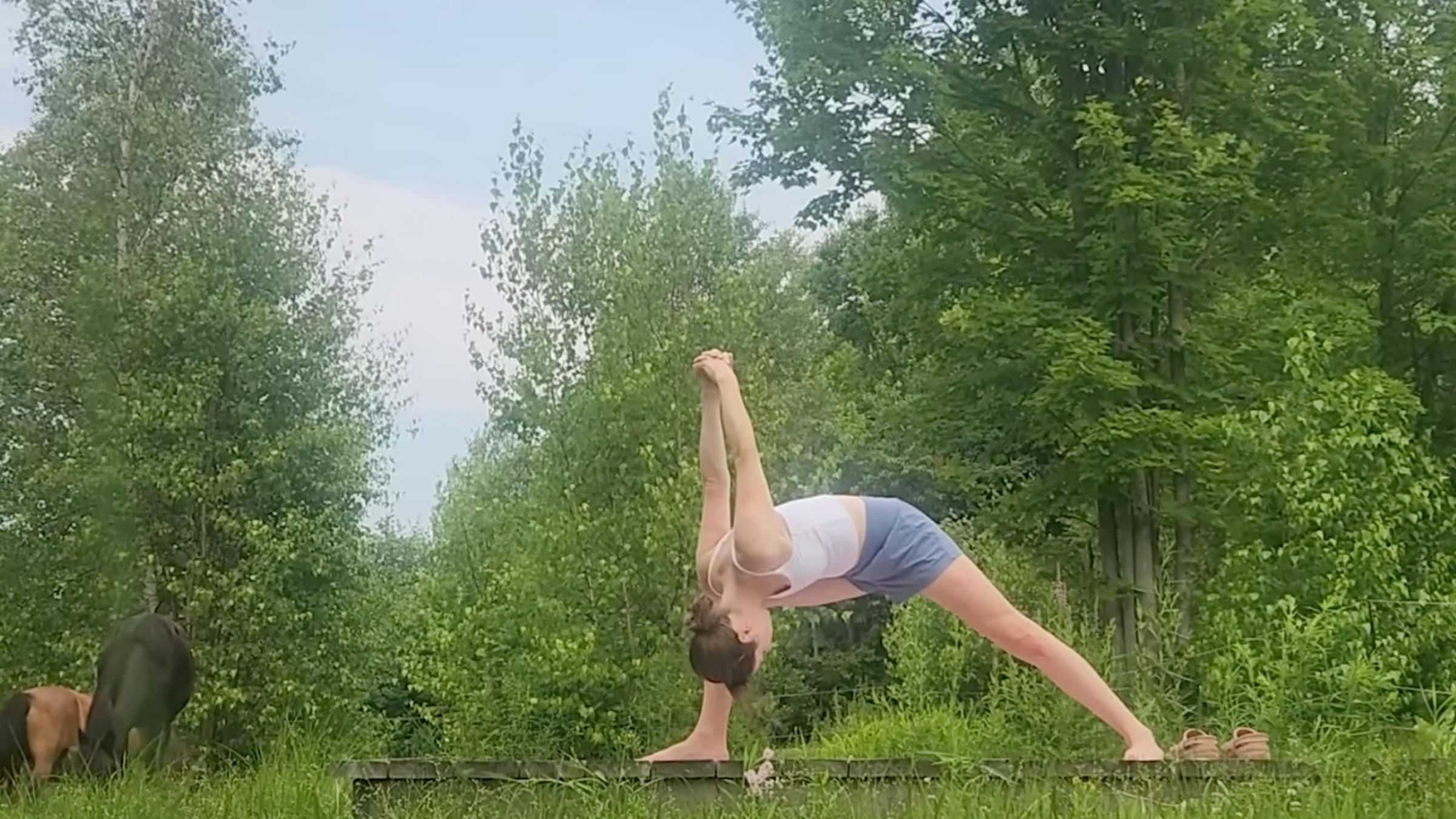 woman in humble warrior pose outside on wooden platform in front of trees and horses