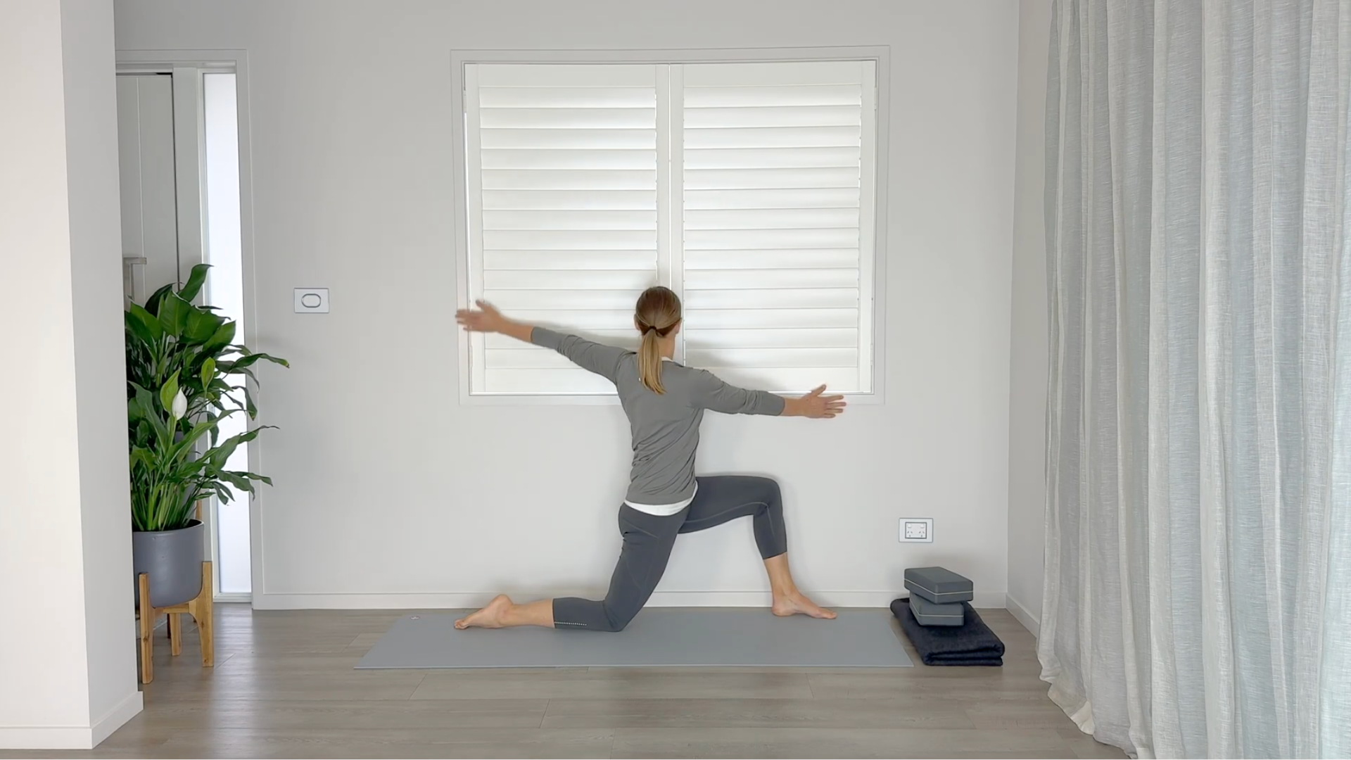 Yoga teacher kneeling in a low lunge twist toward the wall