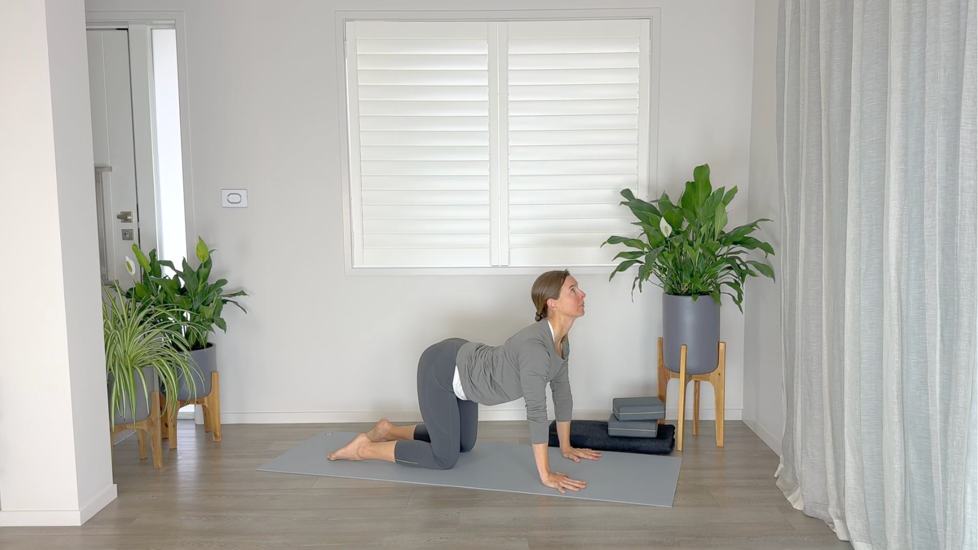 Yoga teacher on a mat on hands and knees in Cow Pose