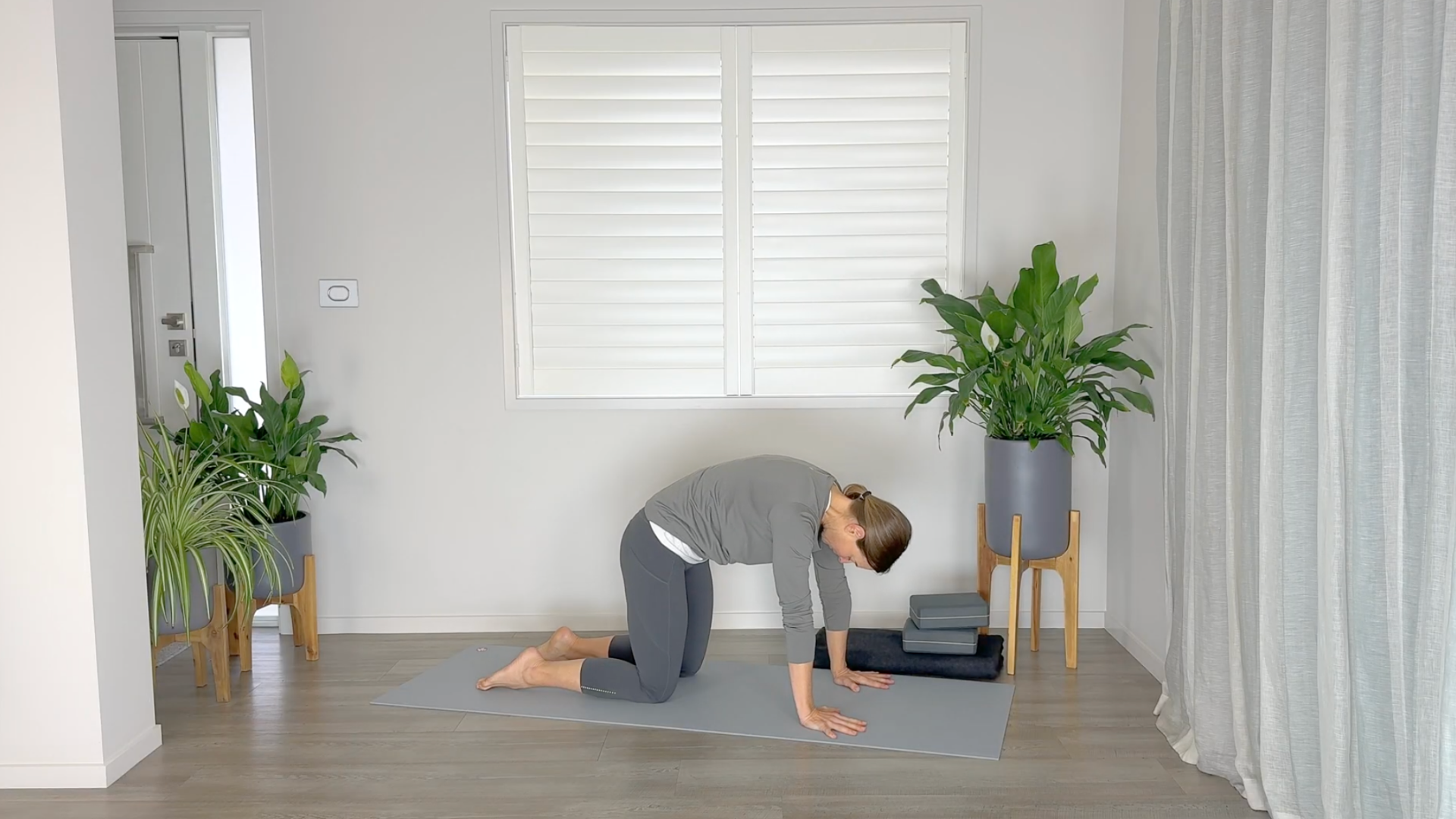 Yoga teacher on hands and knees on a mat in Cat Pose