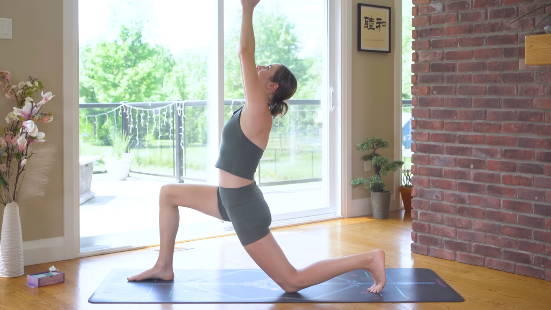 Yoga With Kassandra kneeling on a mat in Low Lunge while bending her elbows and taking a slight backbend