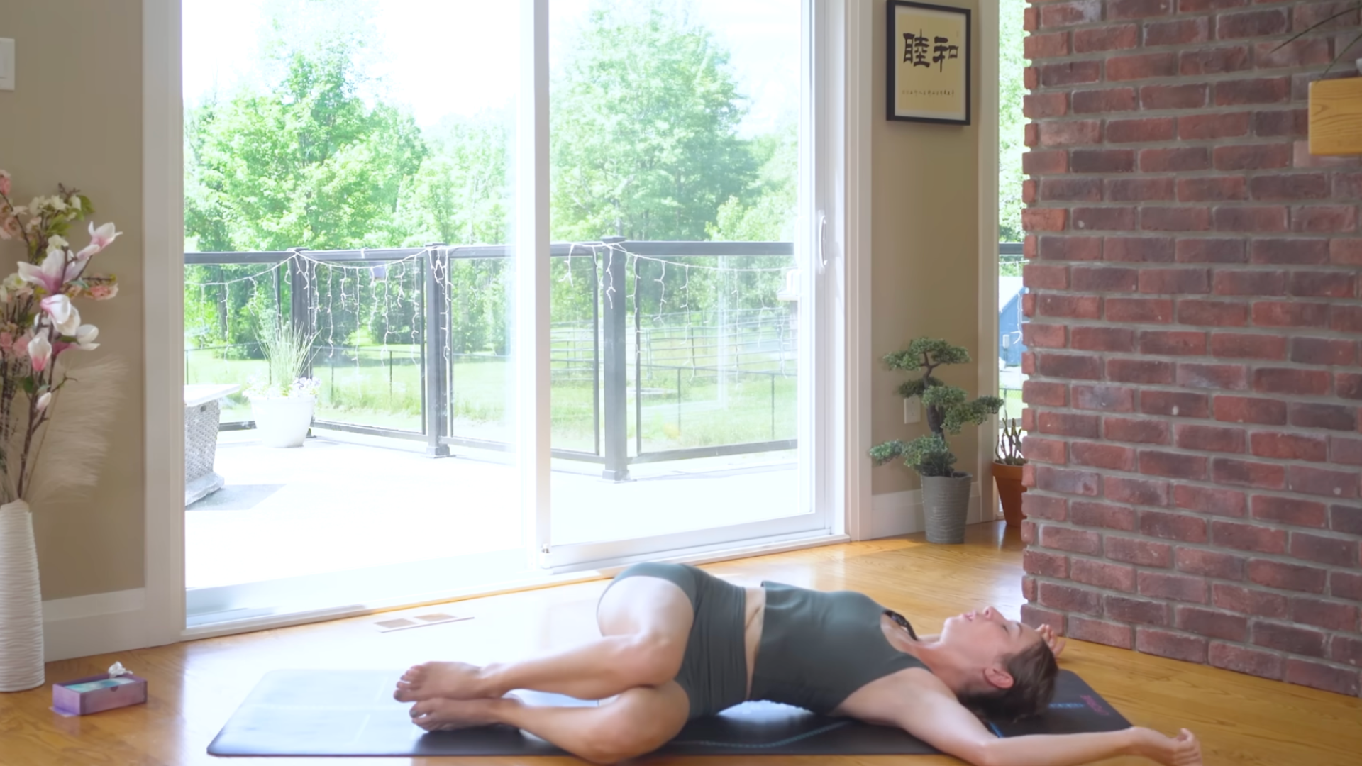 Yoga teacher in a reclined twist on a mat with her knees to the left and her arms straight out from her shoulders