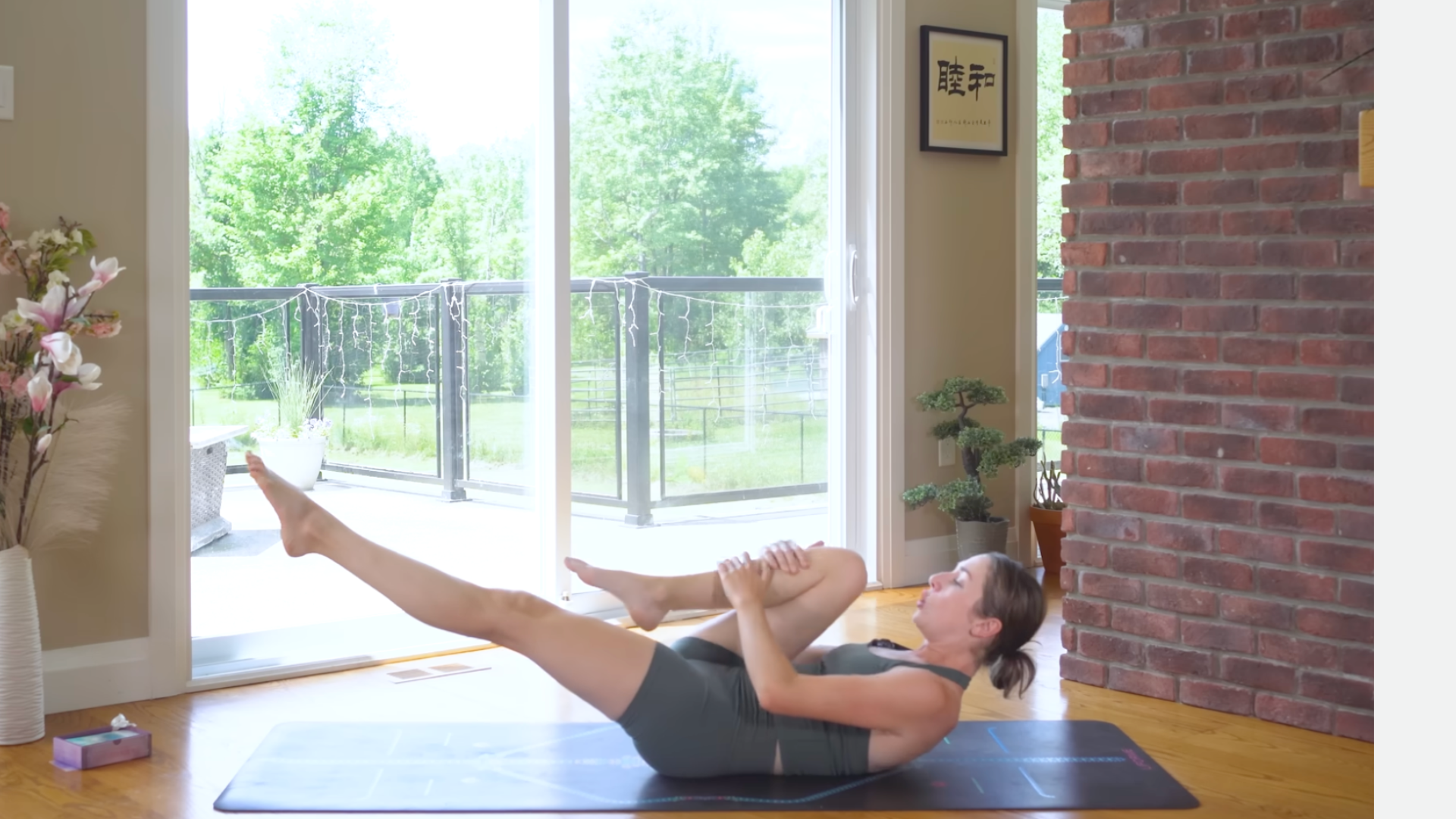Yoga teacher on a mat lying down with her head and shoulders lifted off the mat and her left leg straight with her right knee drawn toward her chest