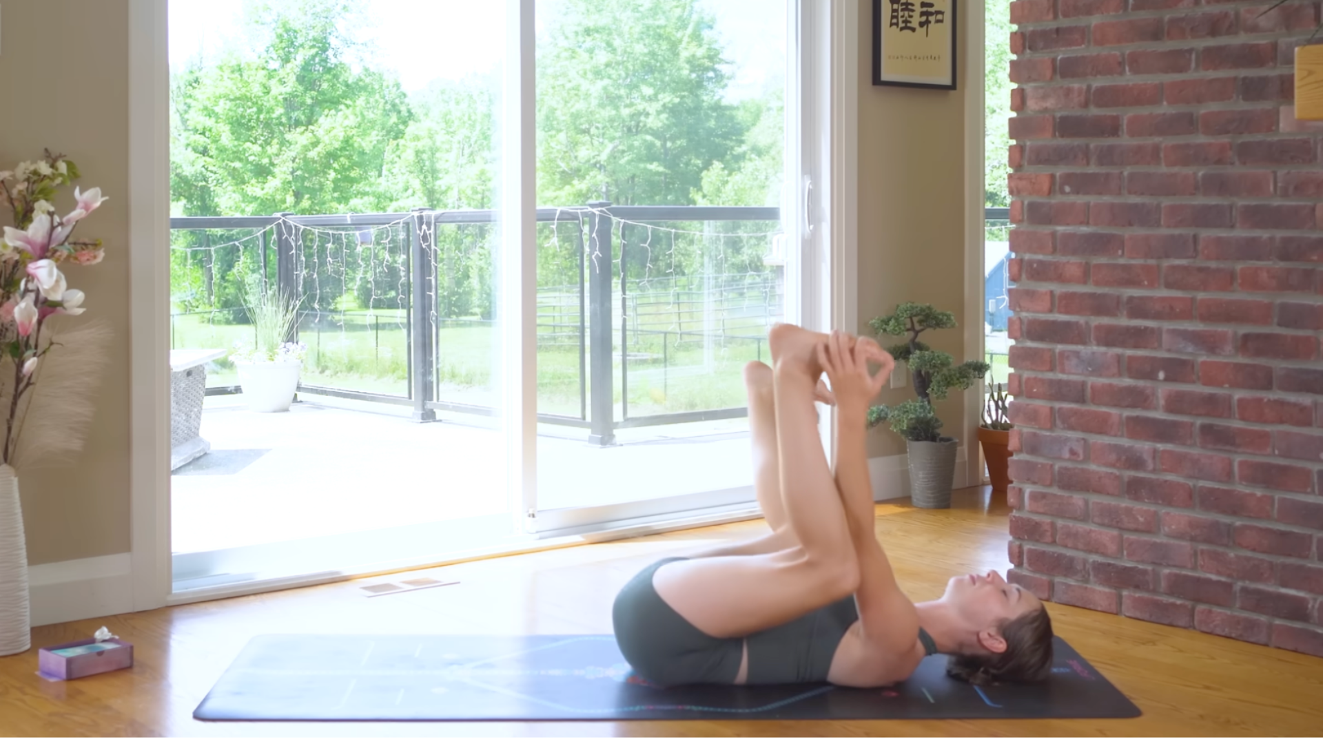 Woman lying on a yoga mat with her knees bent and her ankles stacked over her knees in Happy Baby Pose