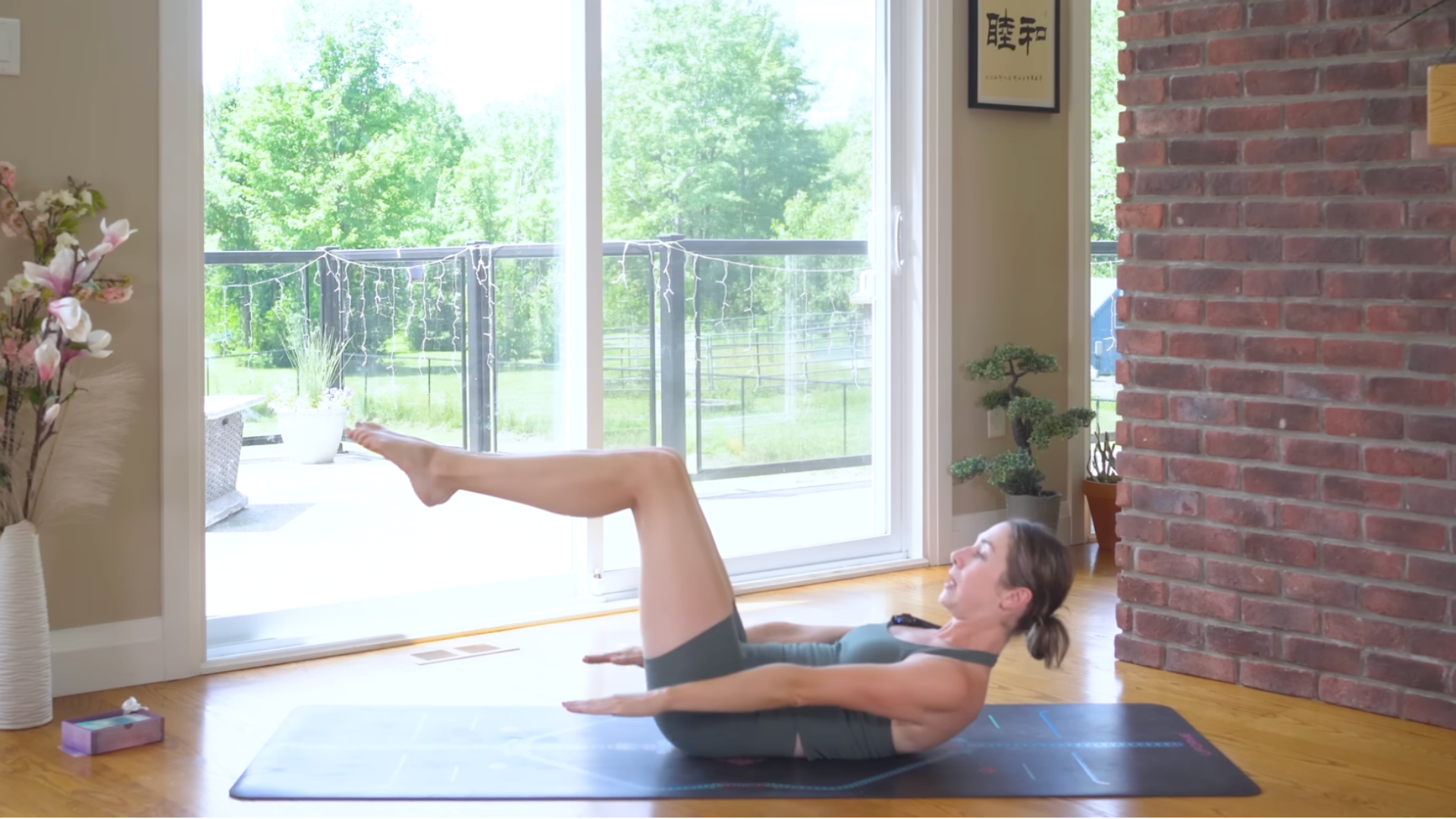 Yoga teacher lying on a mat lifting her head and shoulders and her legs in the pilates core strengthening exercise known as the hundred
