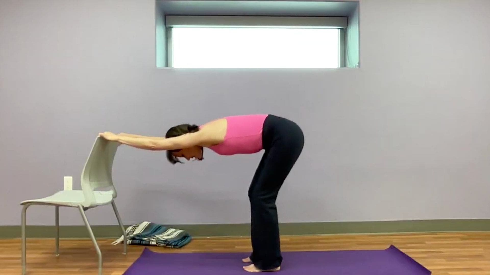 Image of yoga teacher practicing Puppy Pose variation with her hands on the edge of the back of a chair.