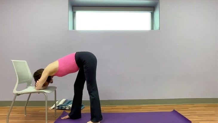 Image of yoga teacher practicing Pyramid Pose variation with her elbows and forearms on the seat of a chair.