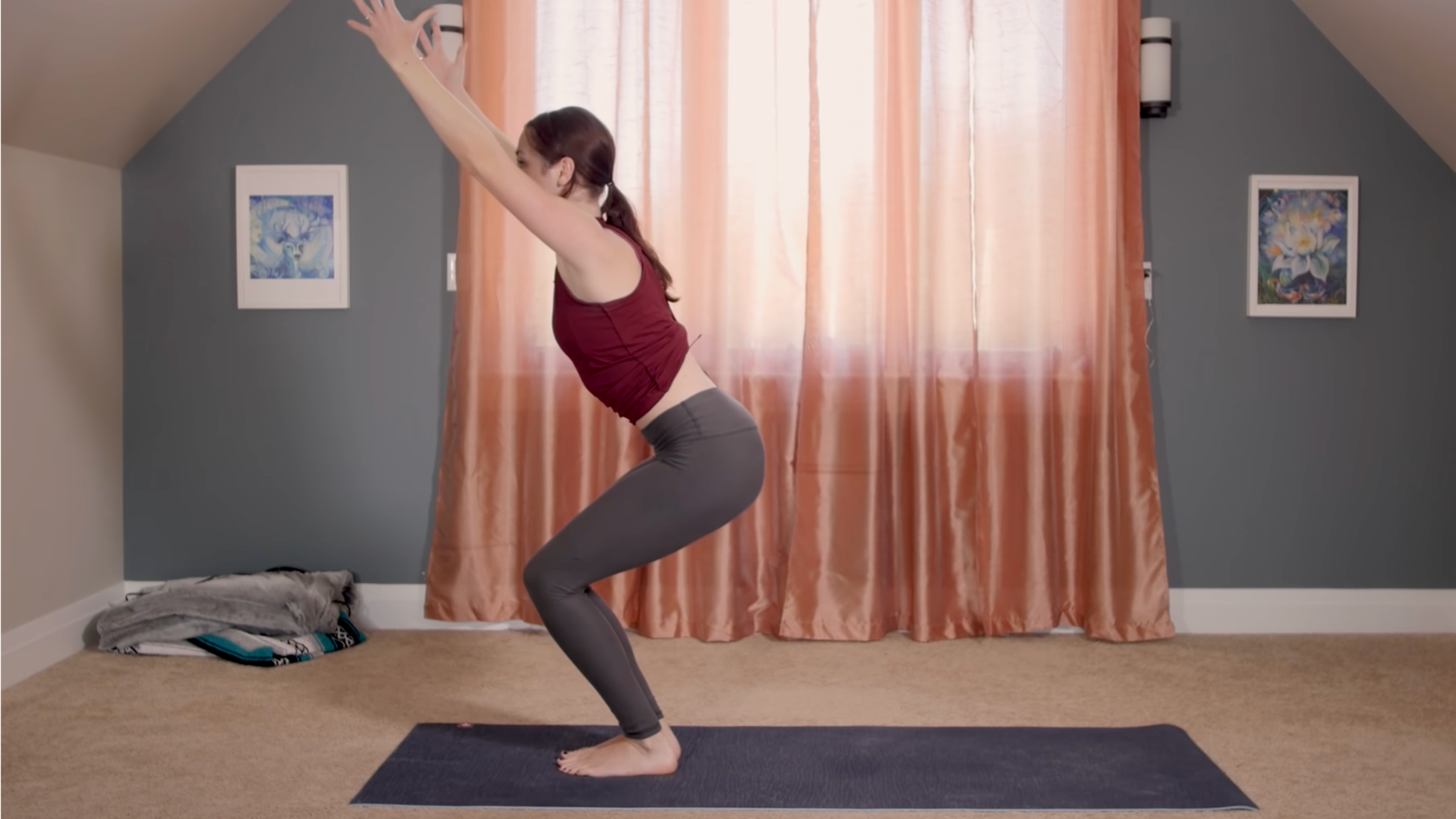 woman in yoga clothes in chair pose on yoga mat in home in front of closed curtains