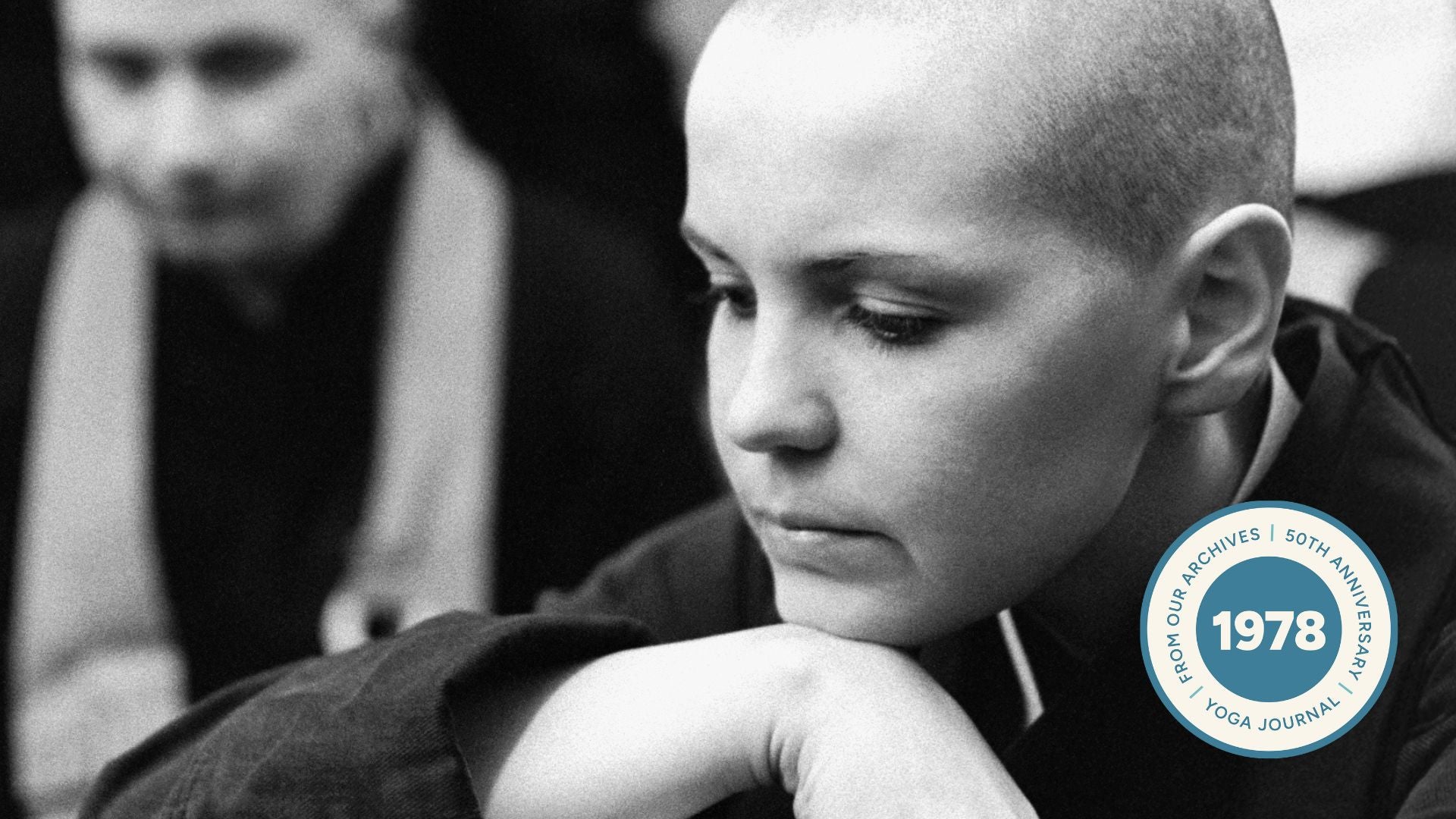Image of female priest in black and white. Her chin is on her hand. A male priest looks at her in the background.