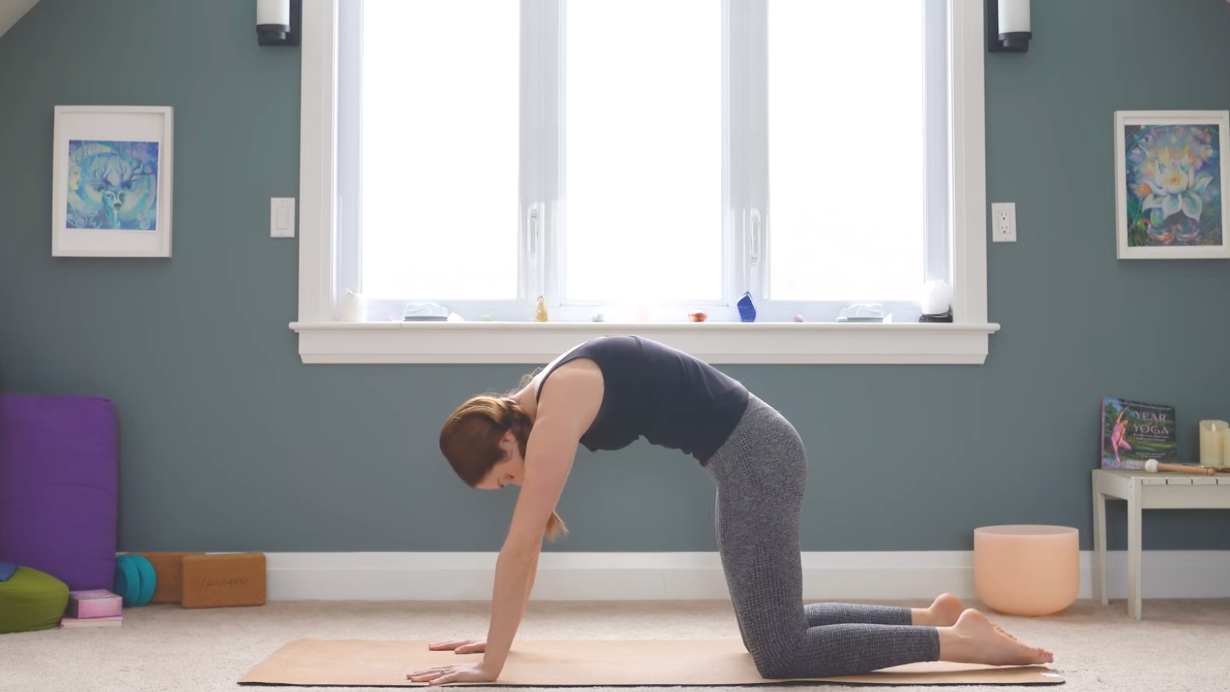 woman on yoga mat in home in cat pose with back arched on all fours