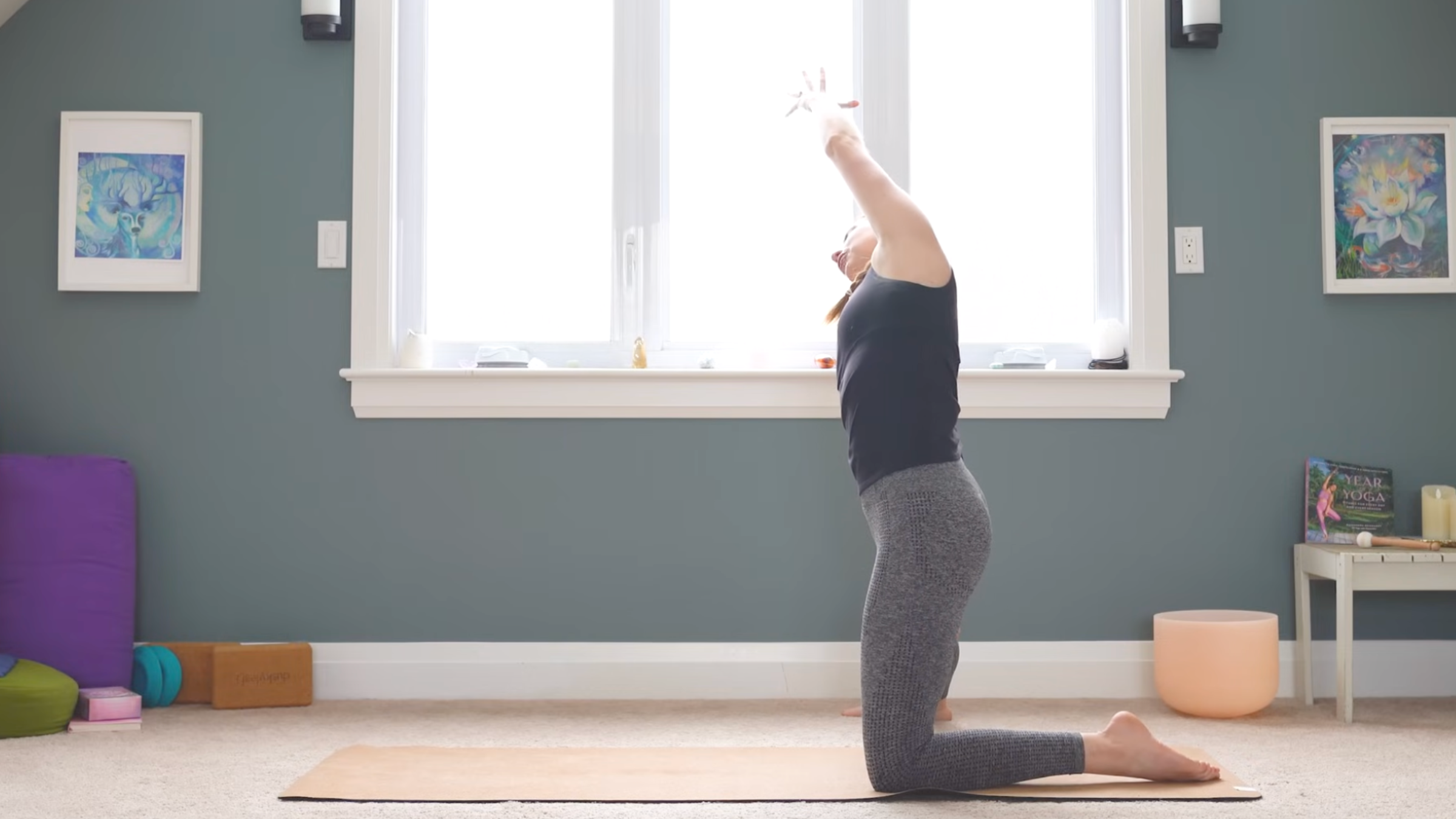 woman on yoga mat in gate pose on left knee with right leg extended to the right side of yoga mat and arms lifted overhead and leaning toward right
