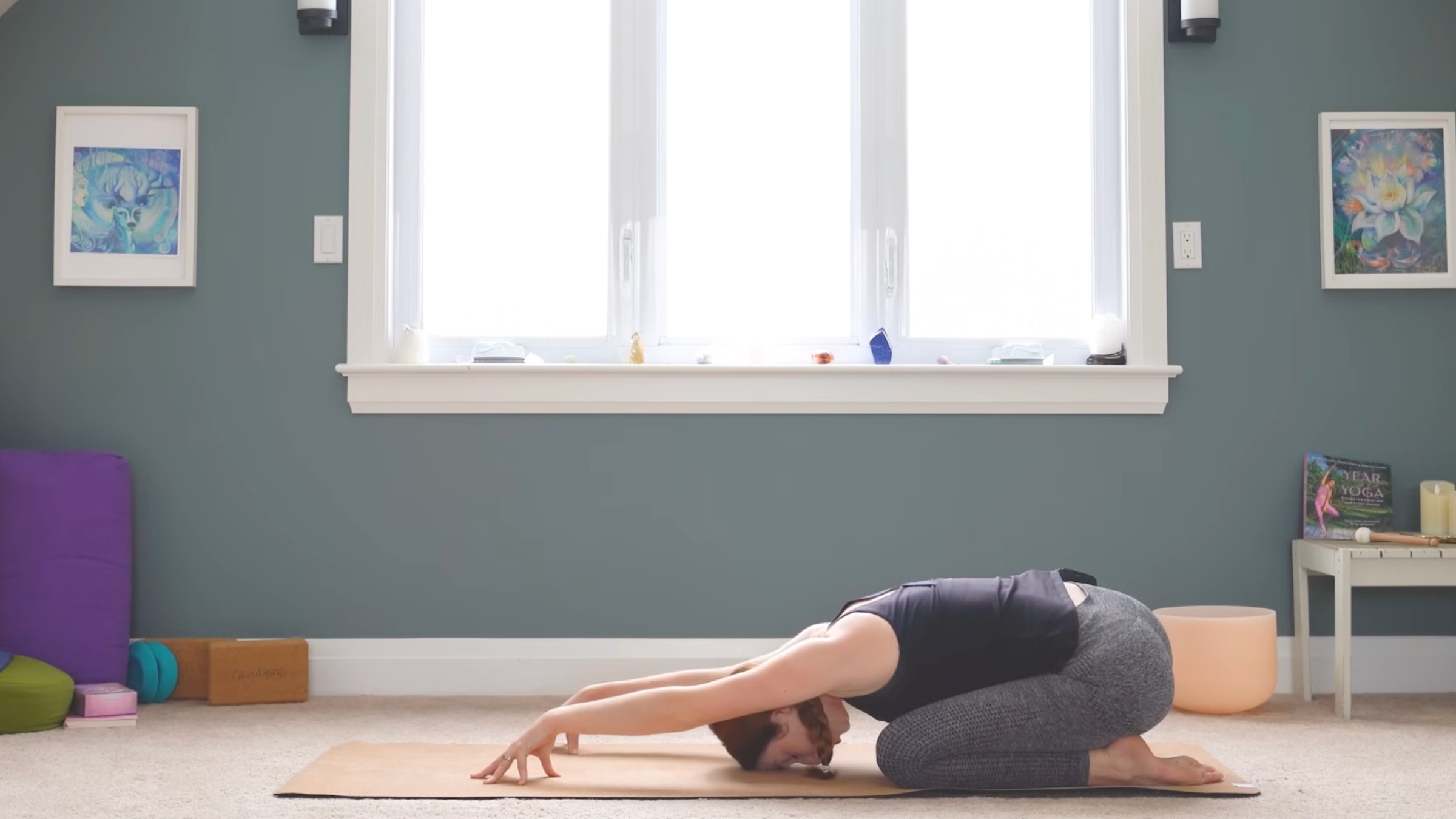woman on yoga mat in child's pose with hands forward and tented, with fingertips touching the mat, and with forehead resting on mat