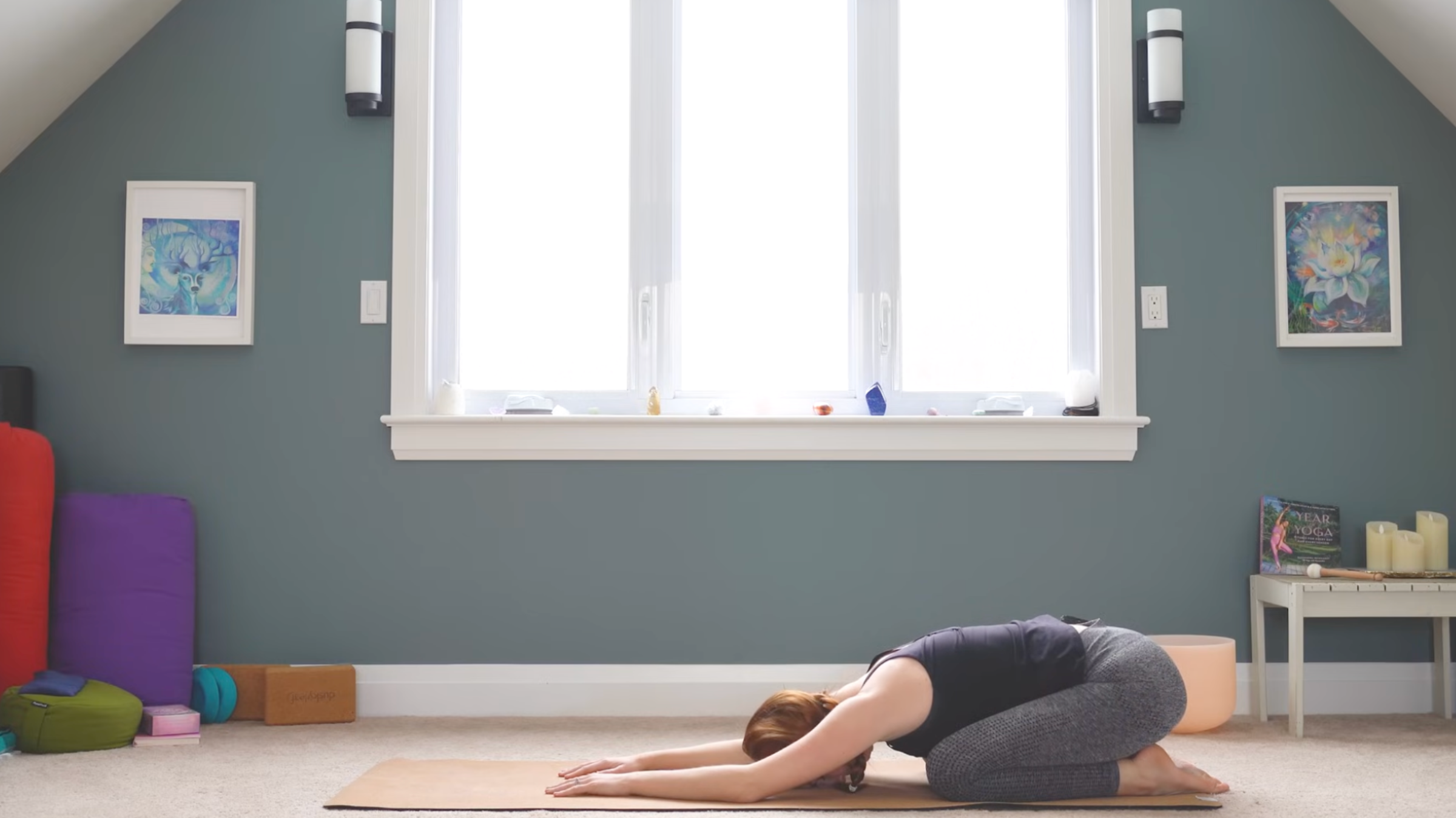woman in child's pose on yoga mat in home in front of windows