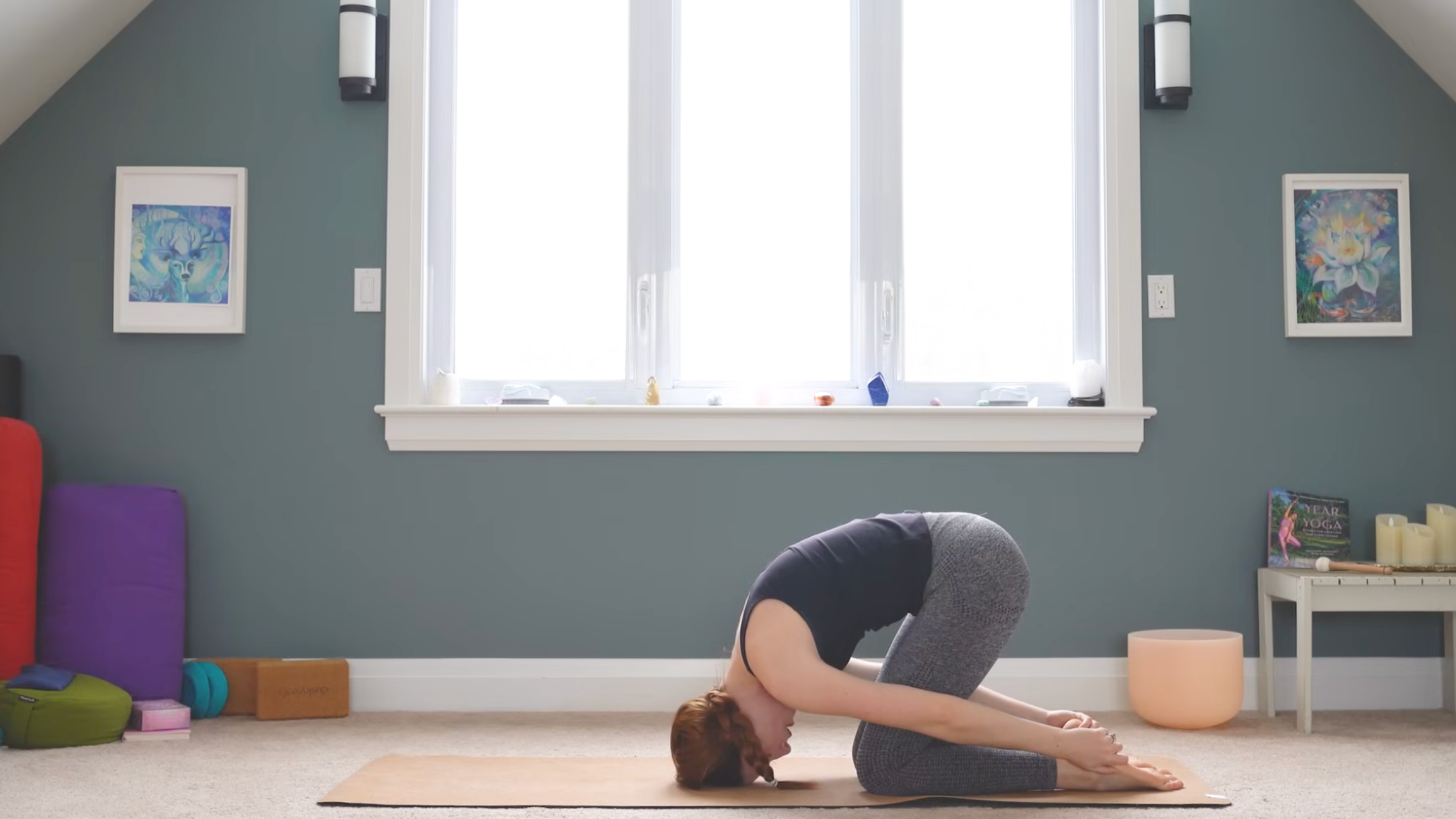 woman in rabbit pose, on knees, forehead on ground, and hands reaching back to grab feet, on yoga mat in home