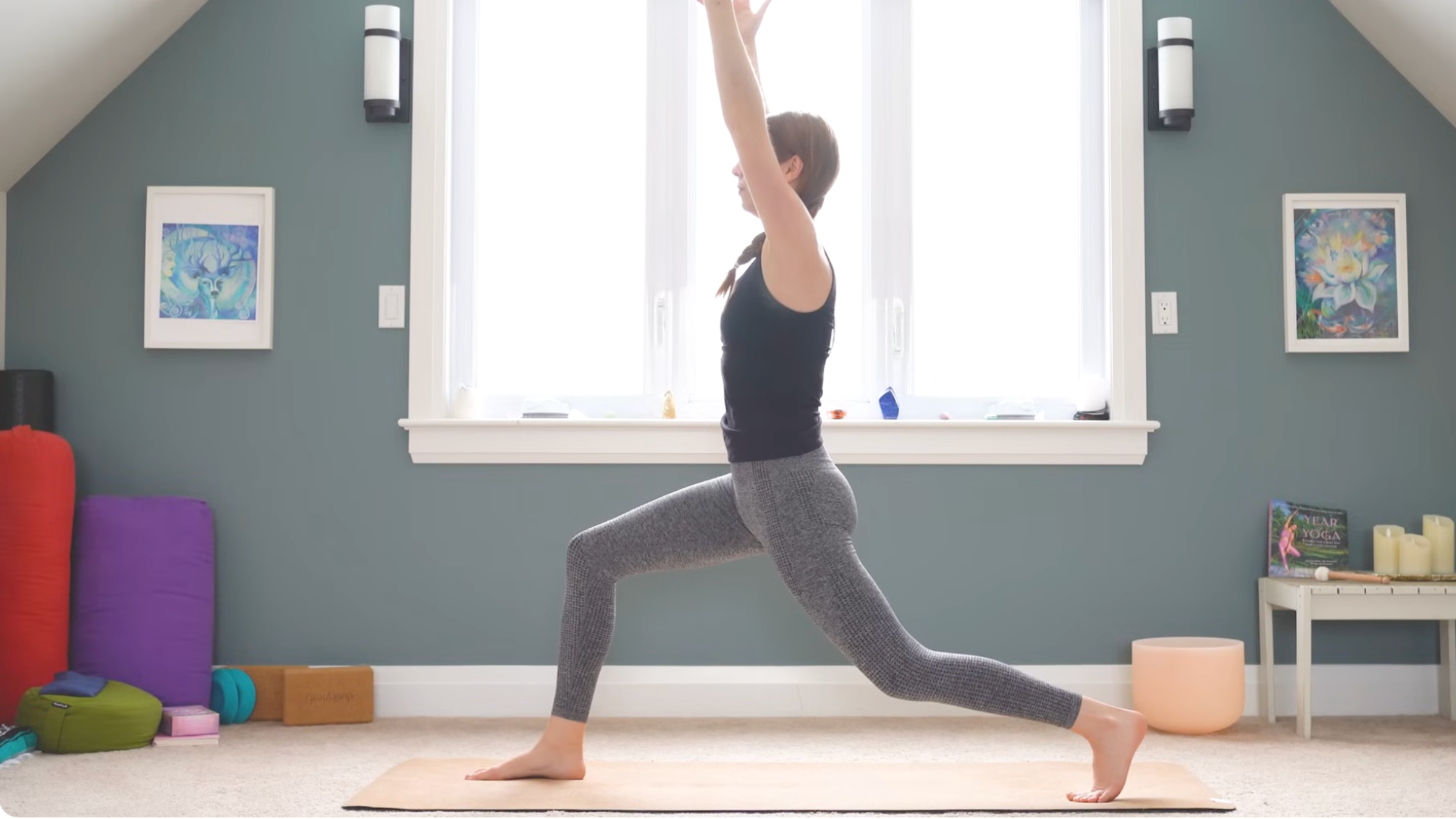 woman in high lunge pose on yoga mat in home with arms extended overhead and right leg forward while practicing anterior pelvic tilt exercises