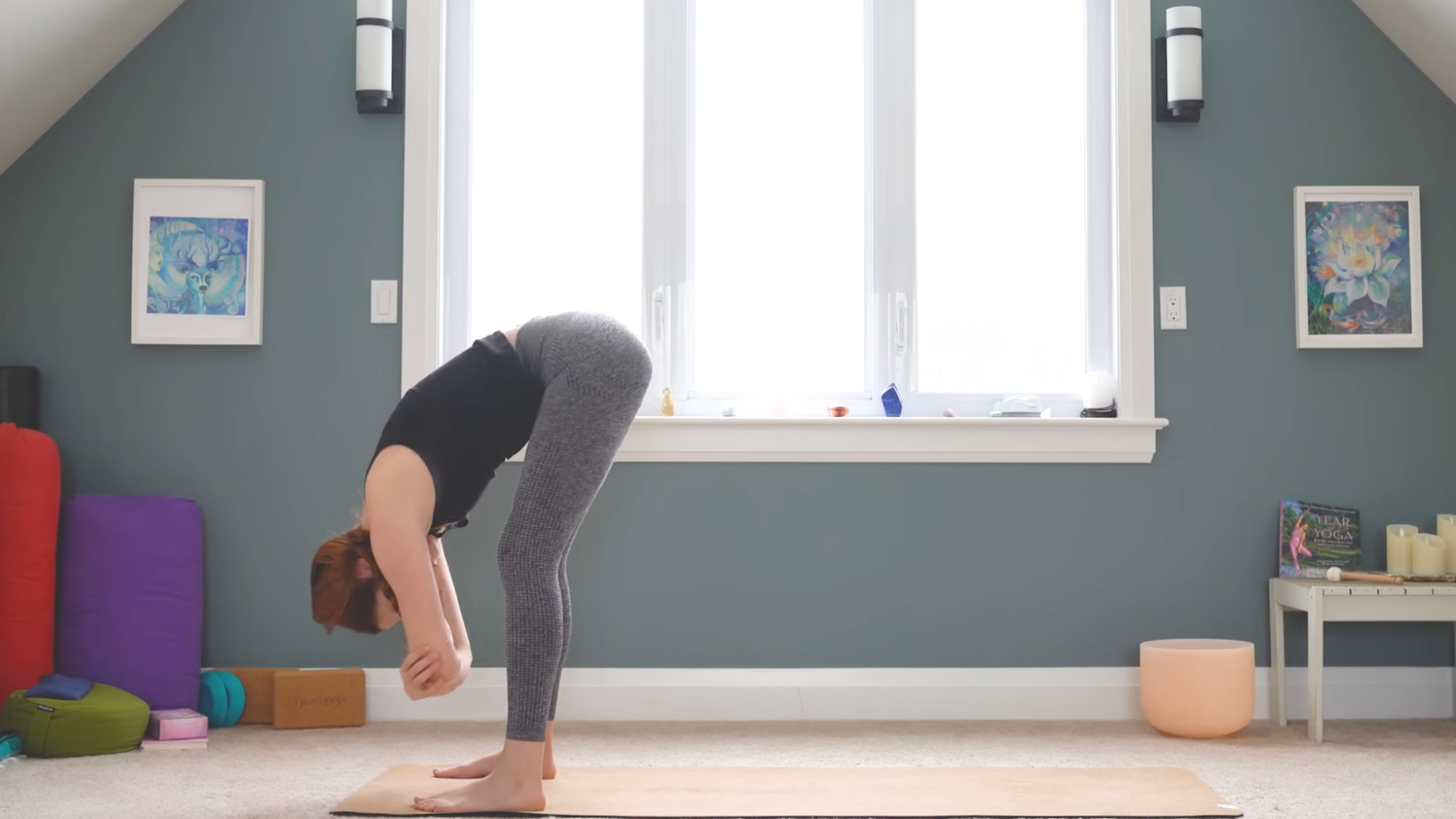 woman in forward fold with arms folded and head relaxed at top of yoga mat in home