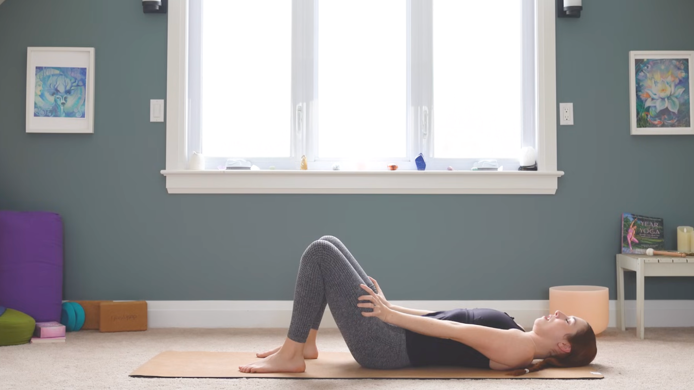 woman lying on back with knees bent, feet on yoga mat and arms straight with hands on thighs while practicing anterior pelvic tilt exercises