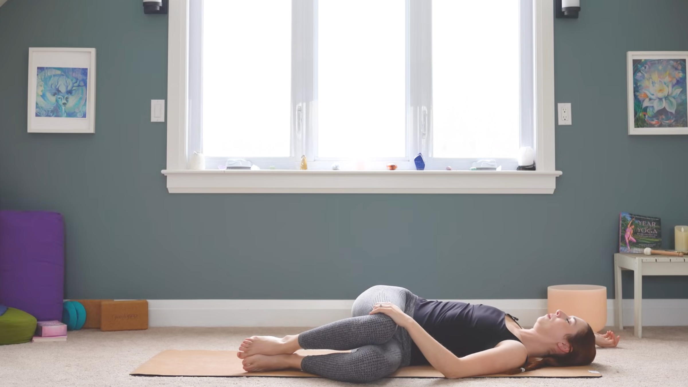 woman in reclined twist pose with both knees together and on left side of yoga mat with back flat on ground while practicing anterior pelvic tilt exercises