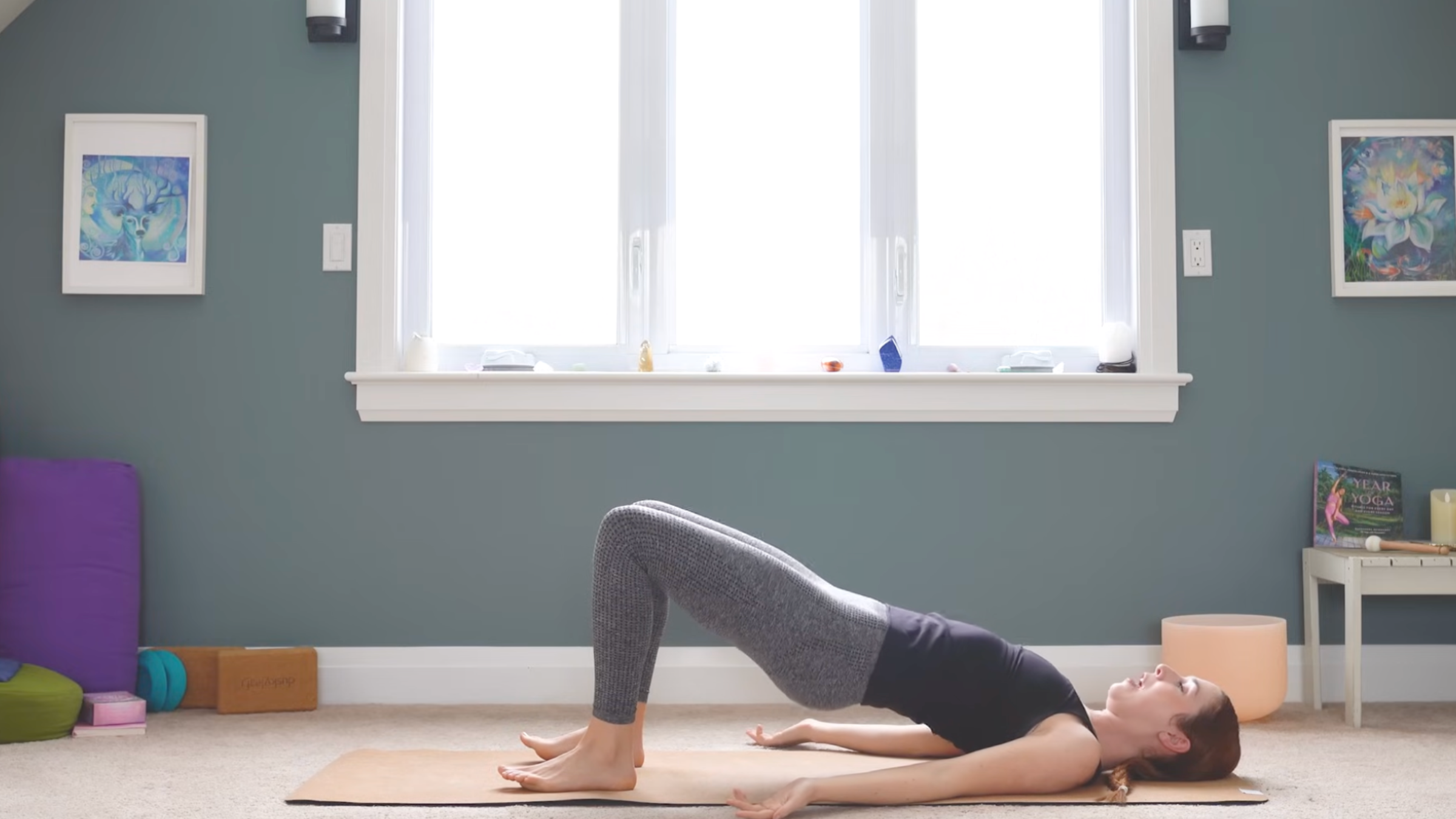 woman in yoga clothes in bridge pose with both feet on mat, knees bent and hips raised toward ceiling on yoga mat in home while practicing anterior pelvic tilt exercises