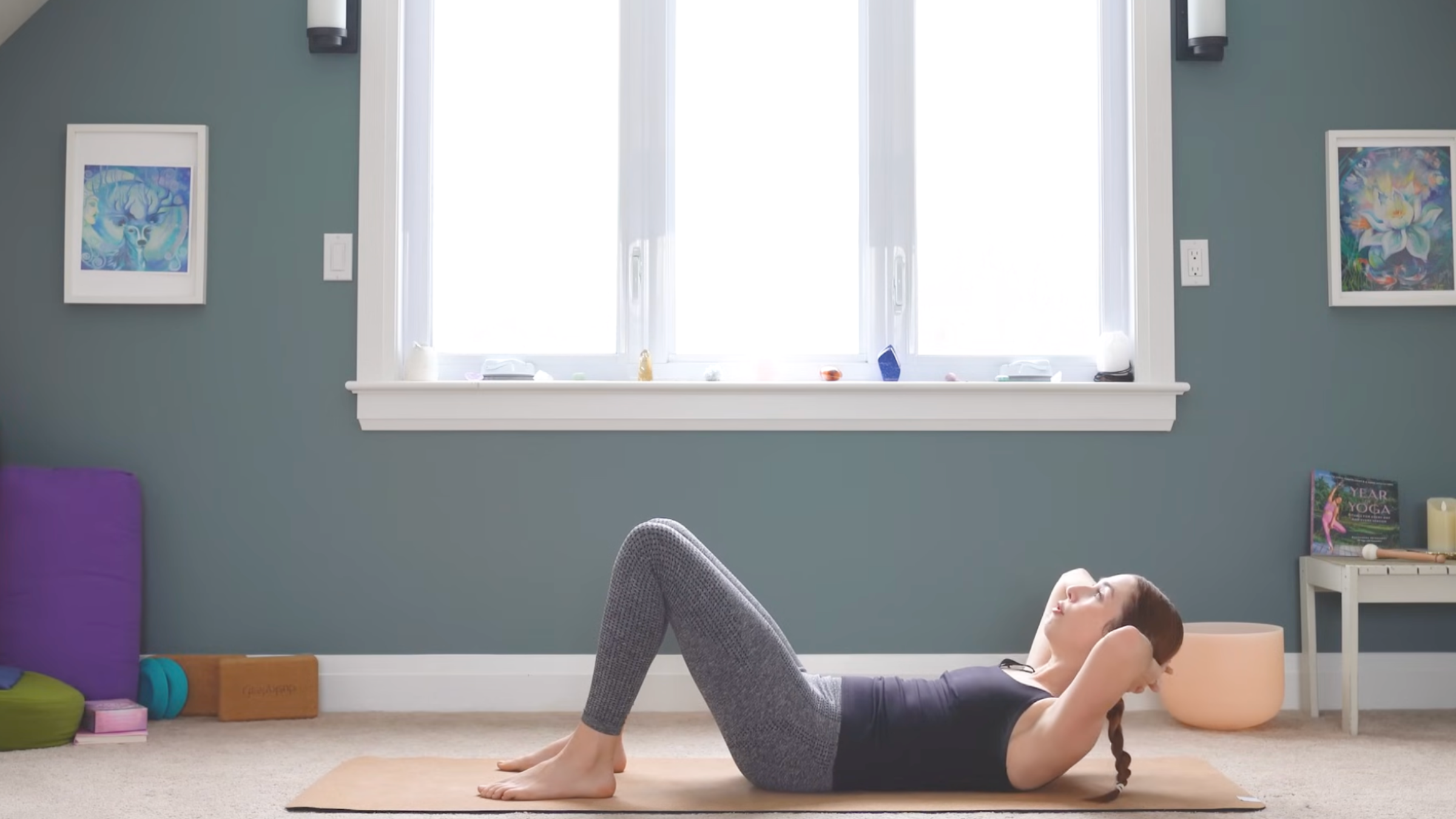 woman in crunch position on floor with fingers interlaced behind head, shoulders and head raised up, knees bent and feet on yoga mat in home