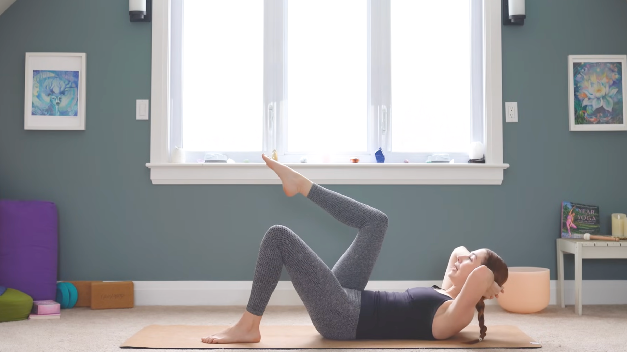 woman in crunch position with hands interlaced behind head, head and shoulders raised off of mat, left foot on mat, and right leg bent with foot point and raised so shin is parallel to the ceiling