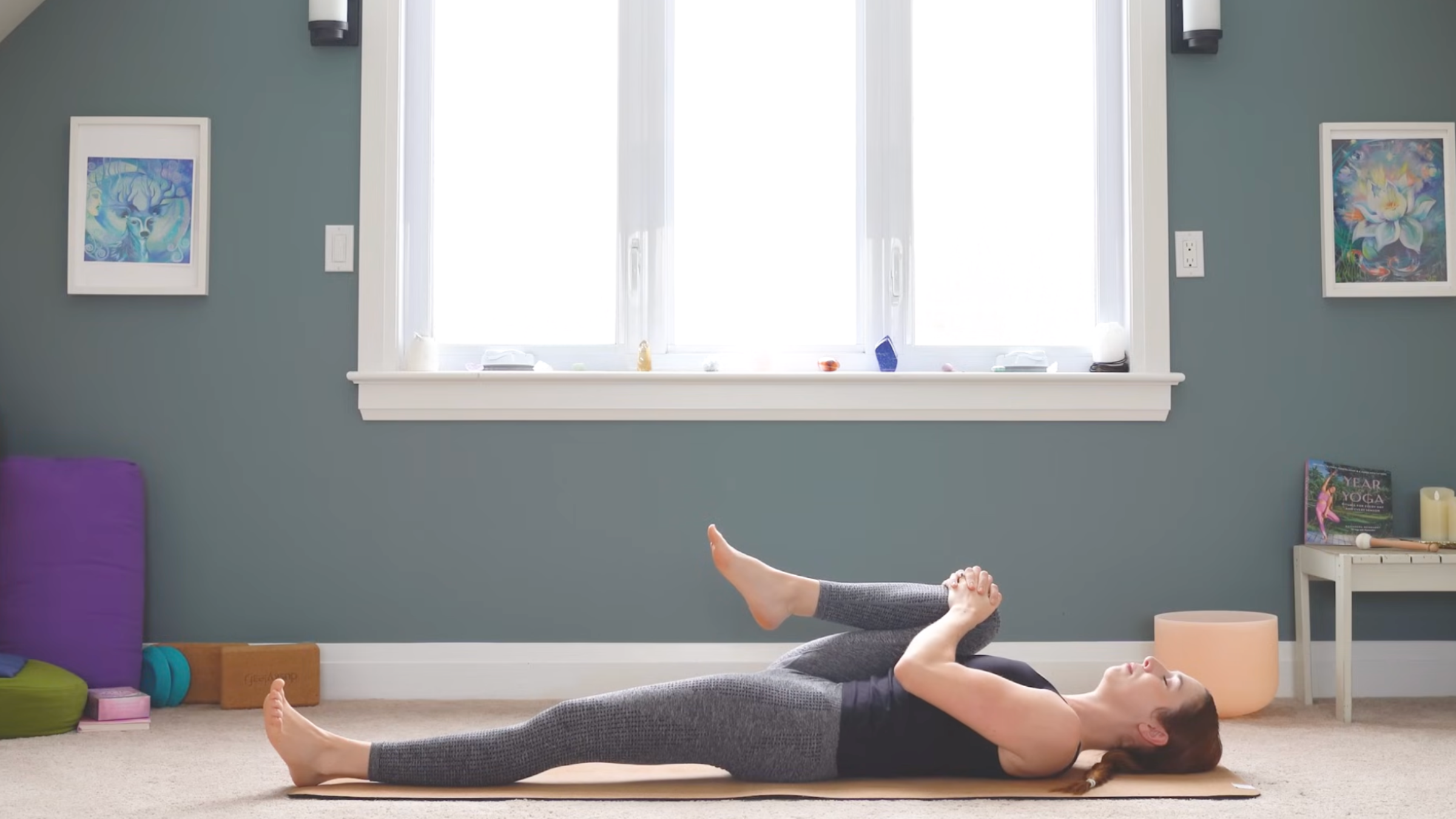 woman lying down on yoga mat with left leg extended long and right knee hugged up to chest in hip flexor stretch