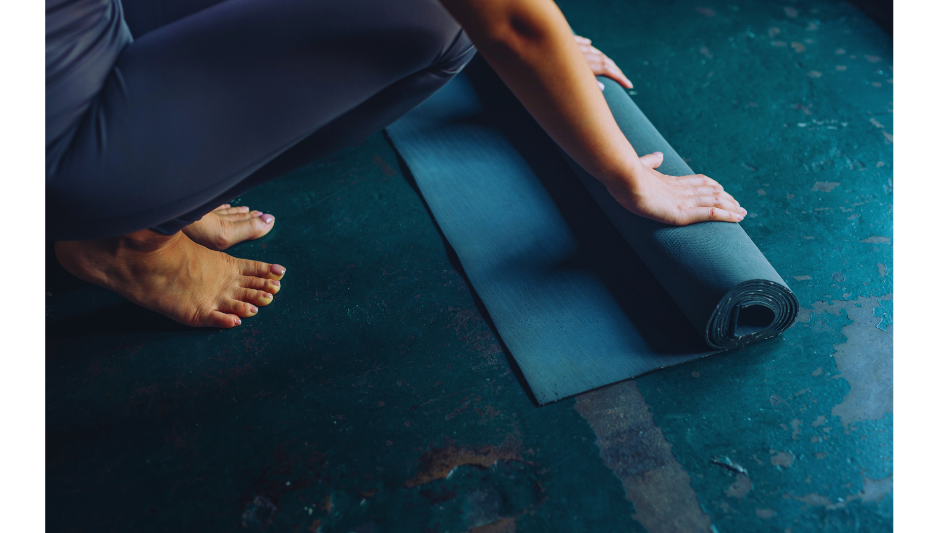 Beginner yoga student unrolling a mat on a concrete studio floor before taking their first class
