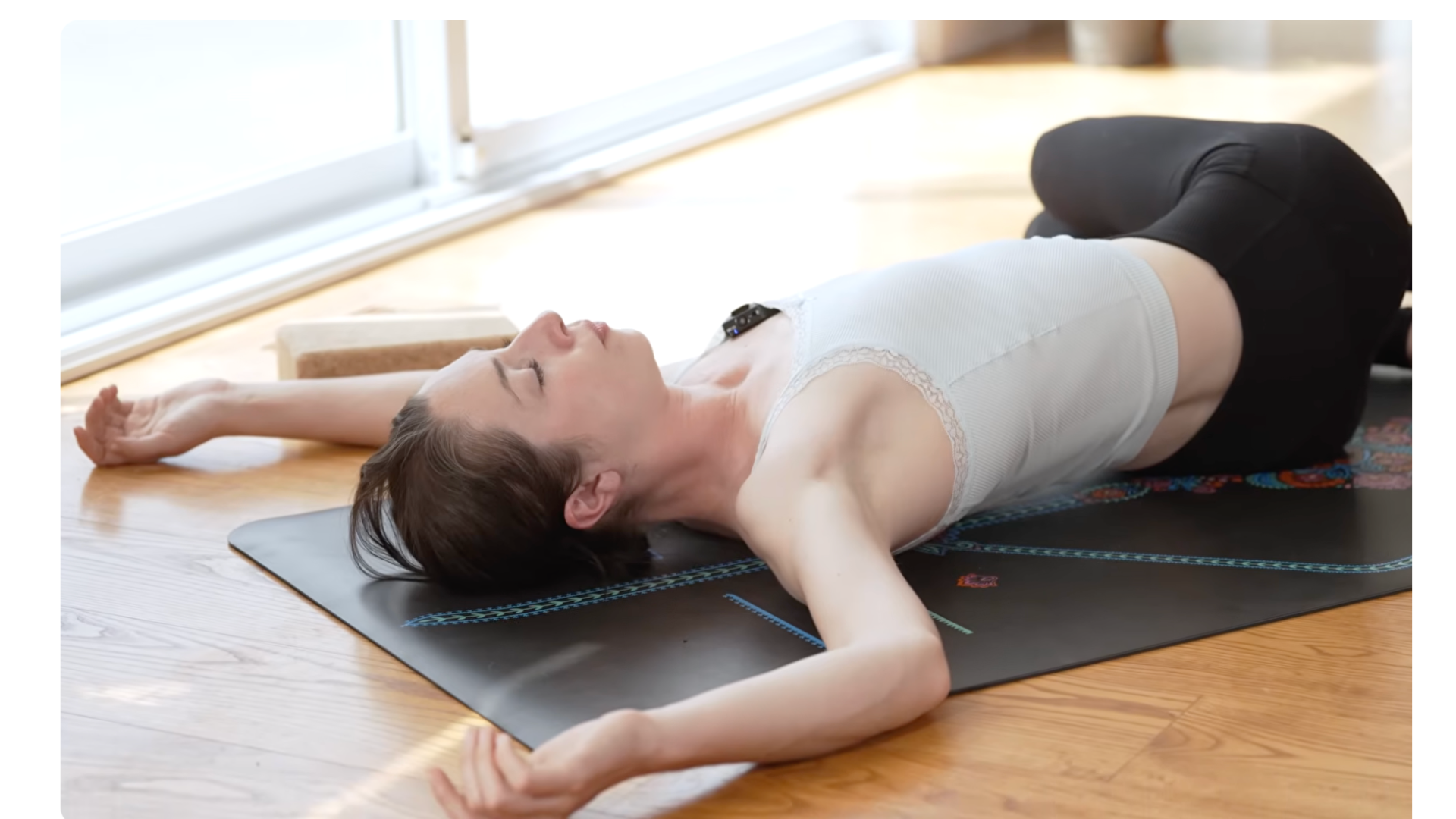 yoga teacher lying on a mat with her knees bent and lowered to one side in a twist