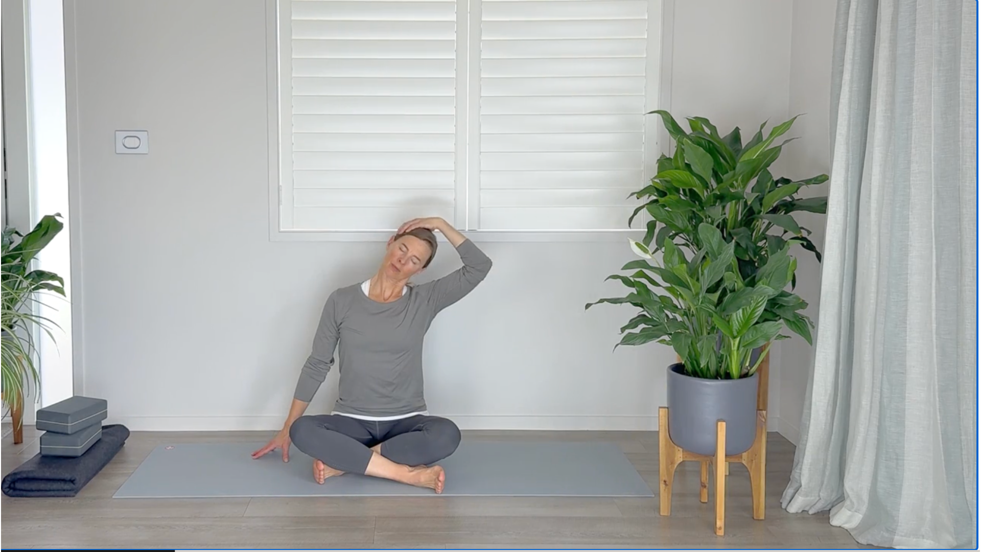 Woman sitting on a yoga mat practicing neck stretches with her hand on the side of her head