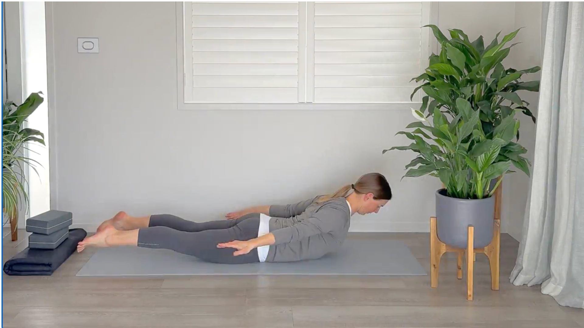 Woman lying on her belly on a yoga mat lifting her head and chest and legs and feet off the mat in Locust Pose