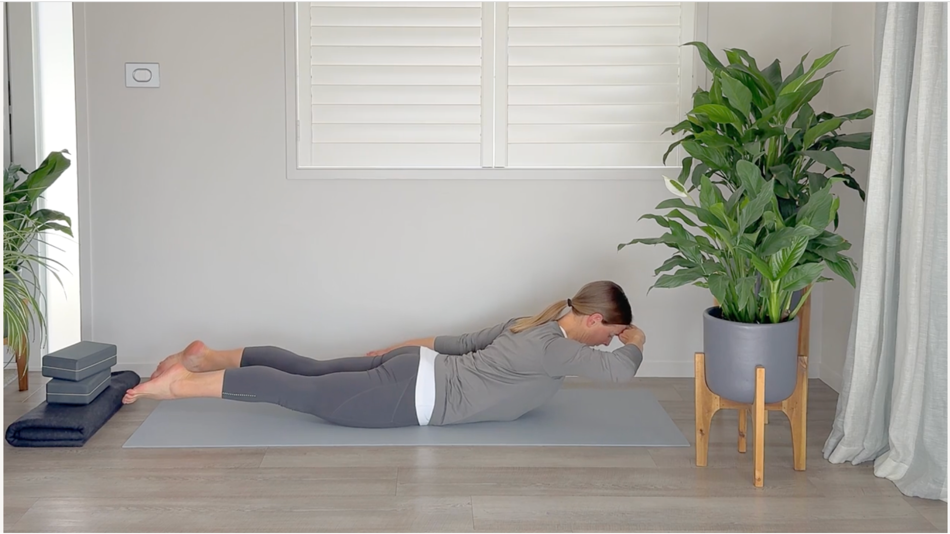 Woman lying belly down on a mat lifting her head and pressing it into her hand