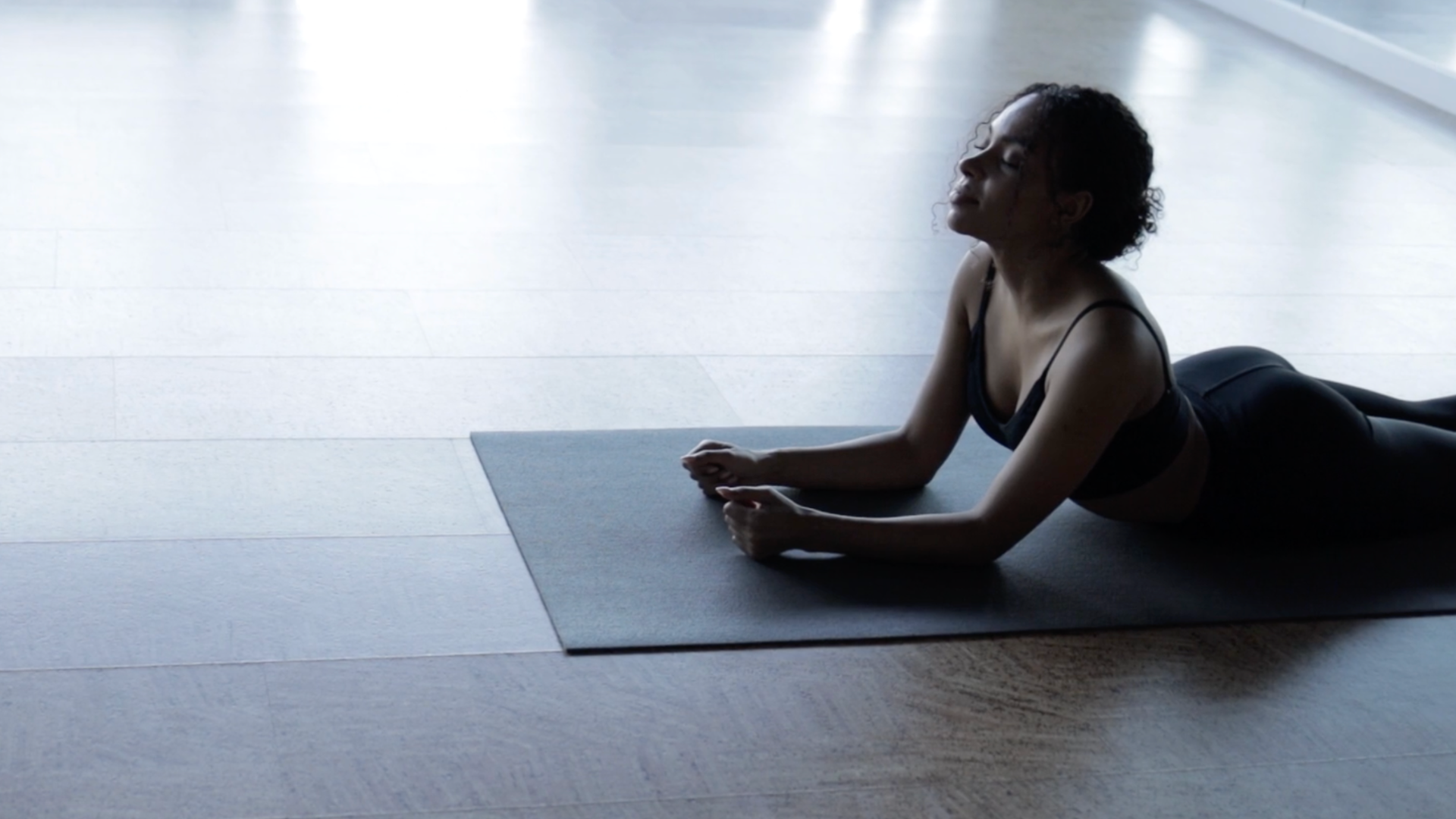 Woman lying on a yoga mat in Sphinx Pose while tilting her head too far back and straining her neck