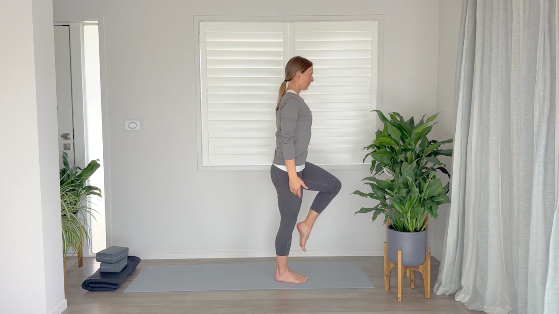 Woman standing on a yoga mat drawing her knee toward her chest as glute-strengthening exercises