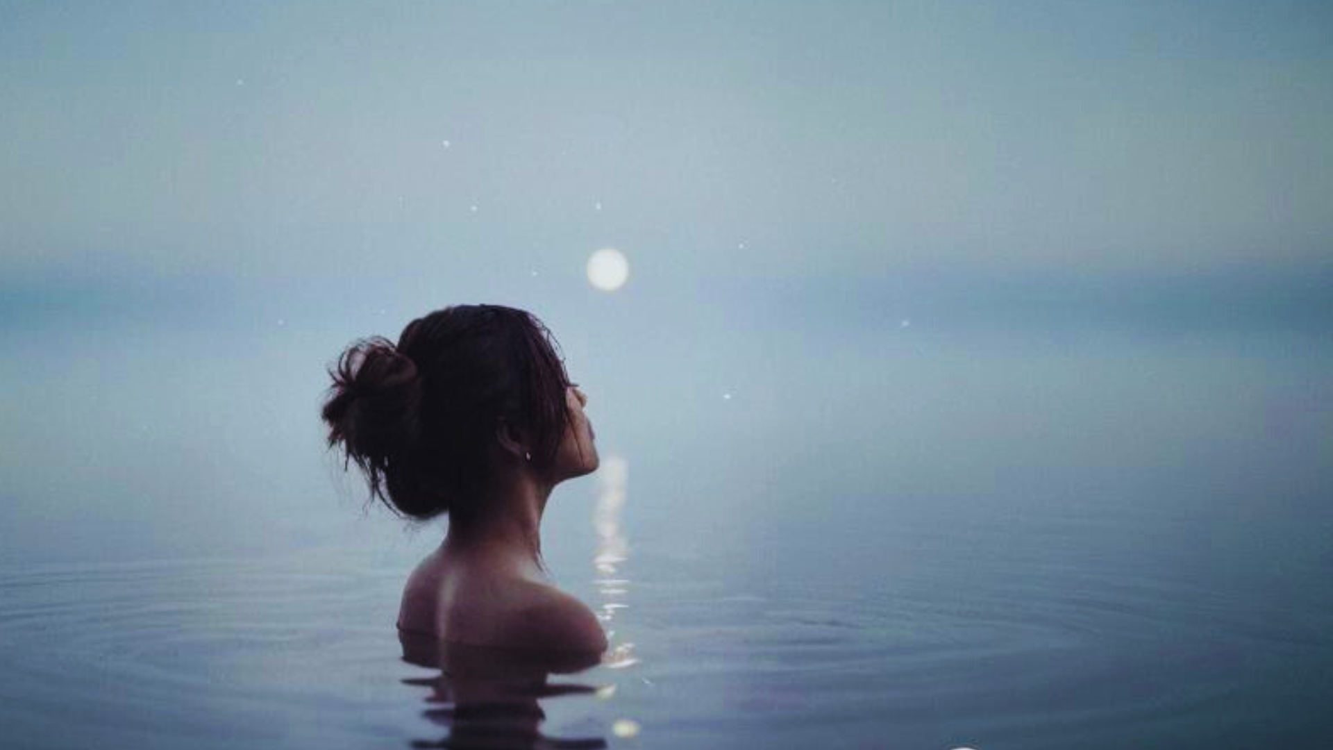 Woman up to her shoulders in water with the lunar eclipse in the background contemplating her weekly horoscope for September 7-13, 2025